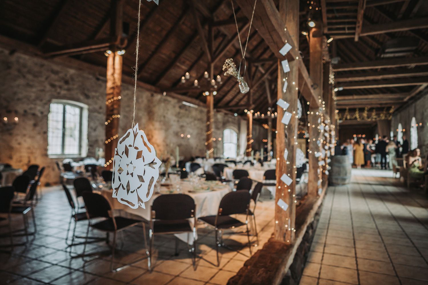 Rustic barn interior decorated with string lights and chandeliers for a romantic wedding reception.