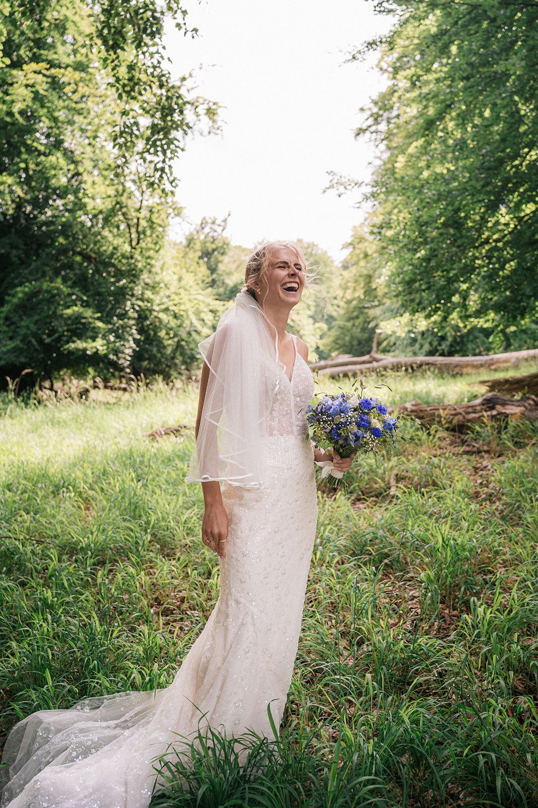 A joyful figure in a flowing white dress twirls through a sunlit meadow holding bright blue cornflowers.