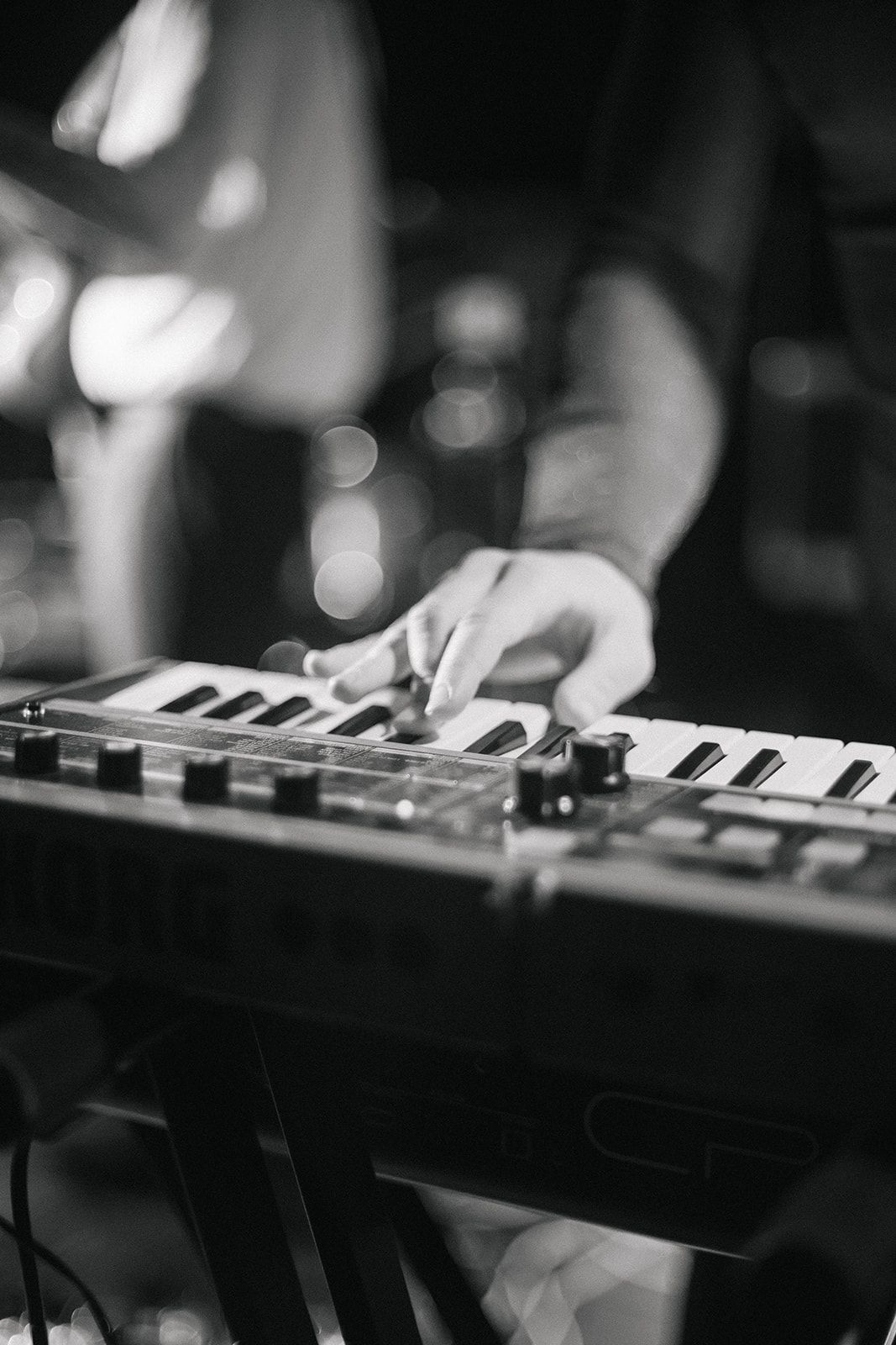 Black and white close-up of hands playing piano keys on a keyboard instrument.