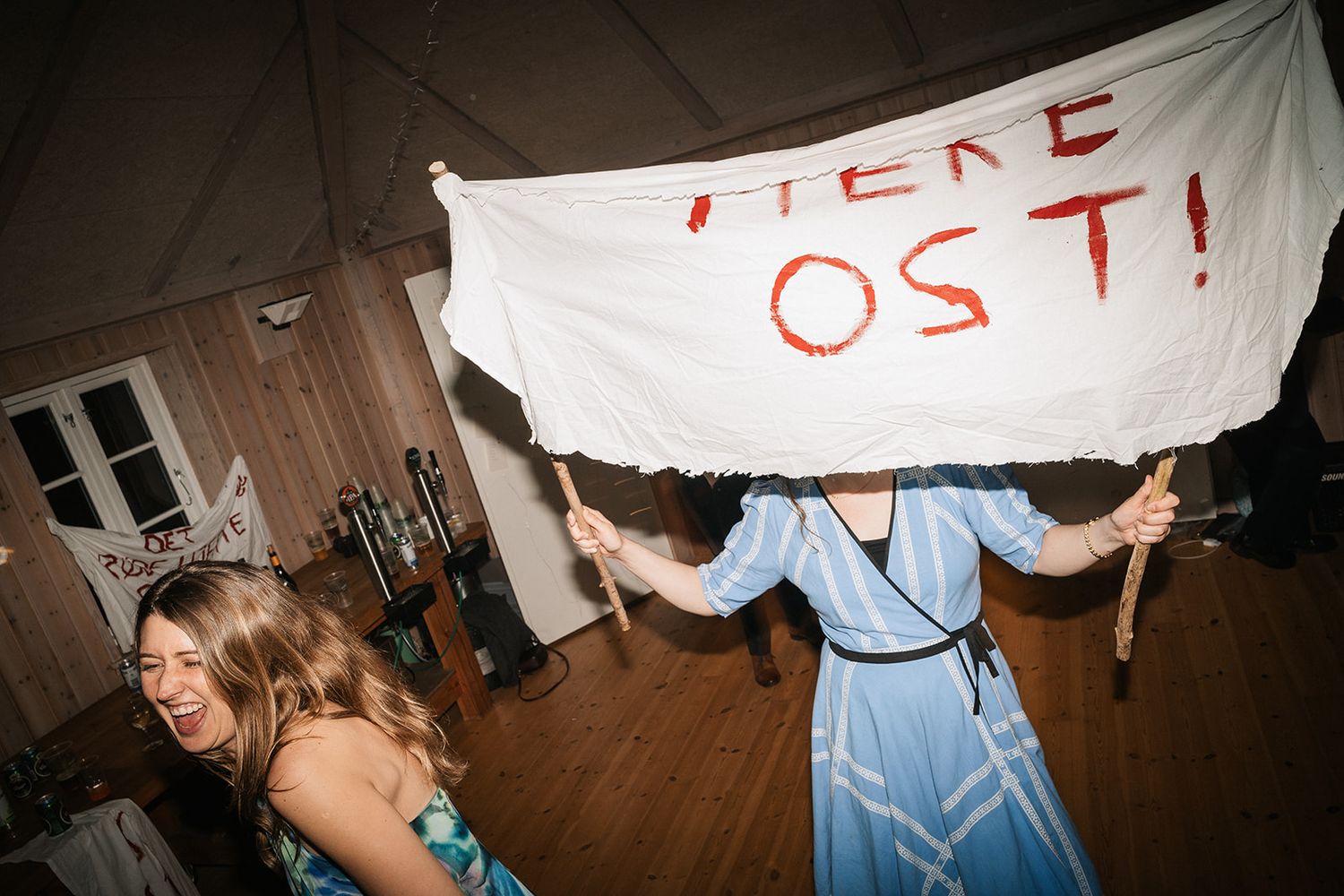 People dance and celebrate at a party while someone holds up a handmade banner with text written in red.