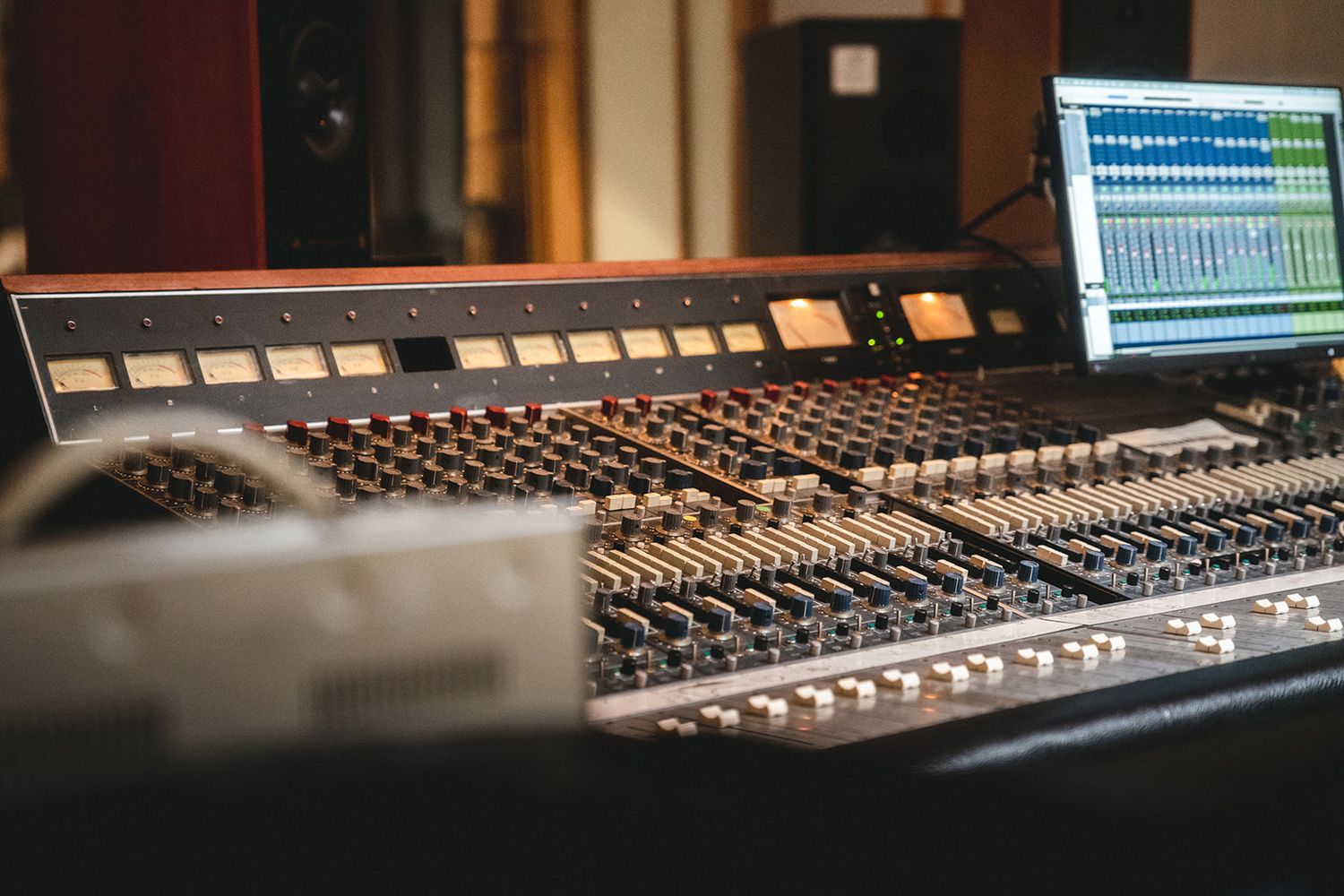 Professional mixing console with illuminated faders and digital audio workstation interface visible in a recording studio setup.
