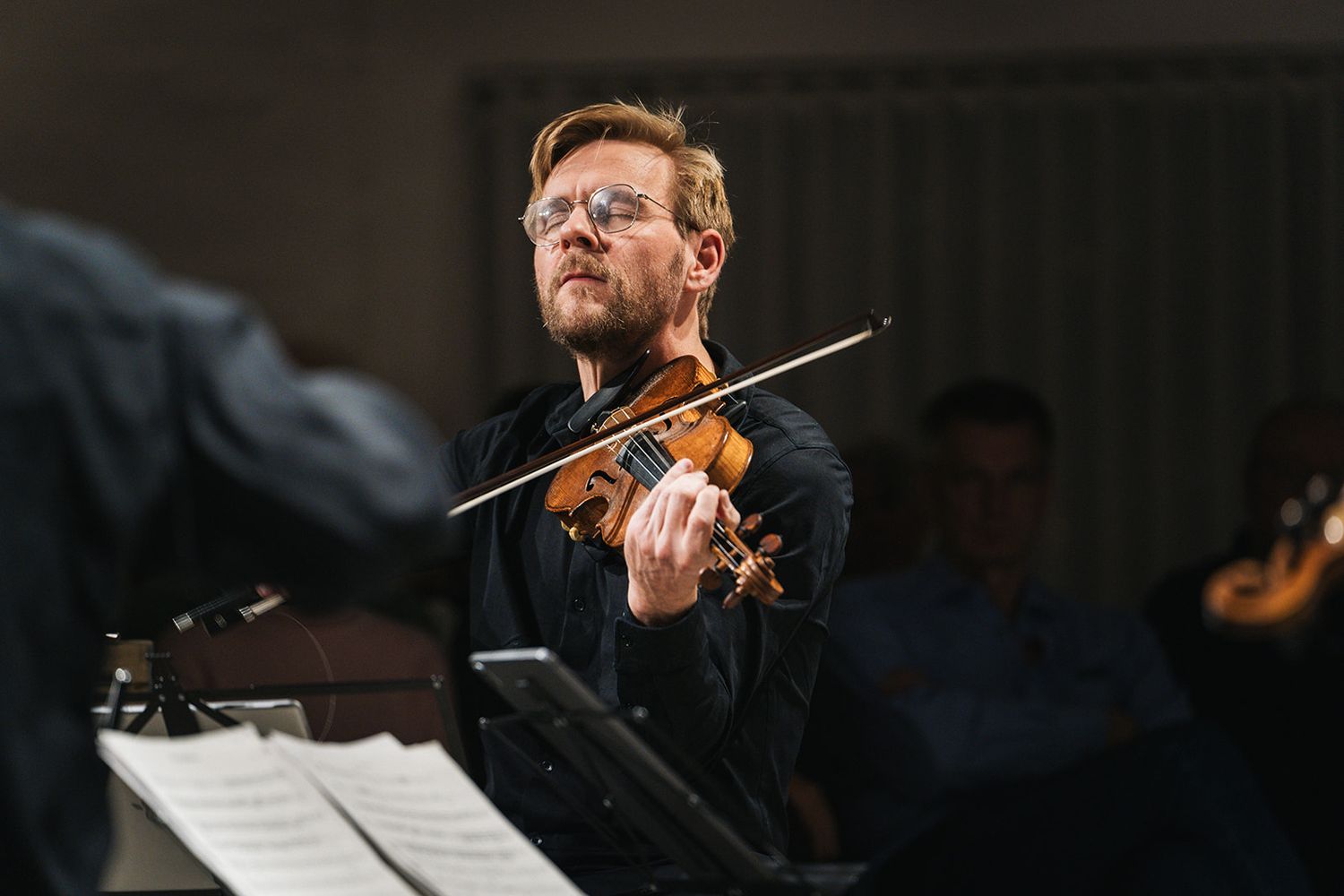 Classical musician performs with violin during an orchestral concert in dramatic lighting.