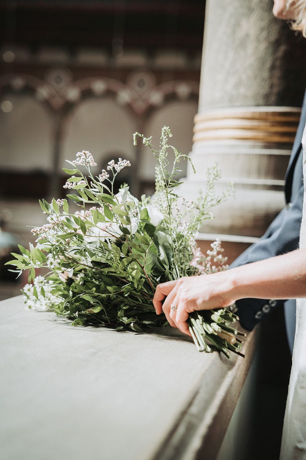 A delicate bouquet of white wildflowers and greenery rests on a stone surface in natural light.