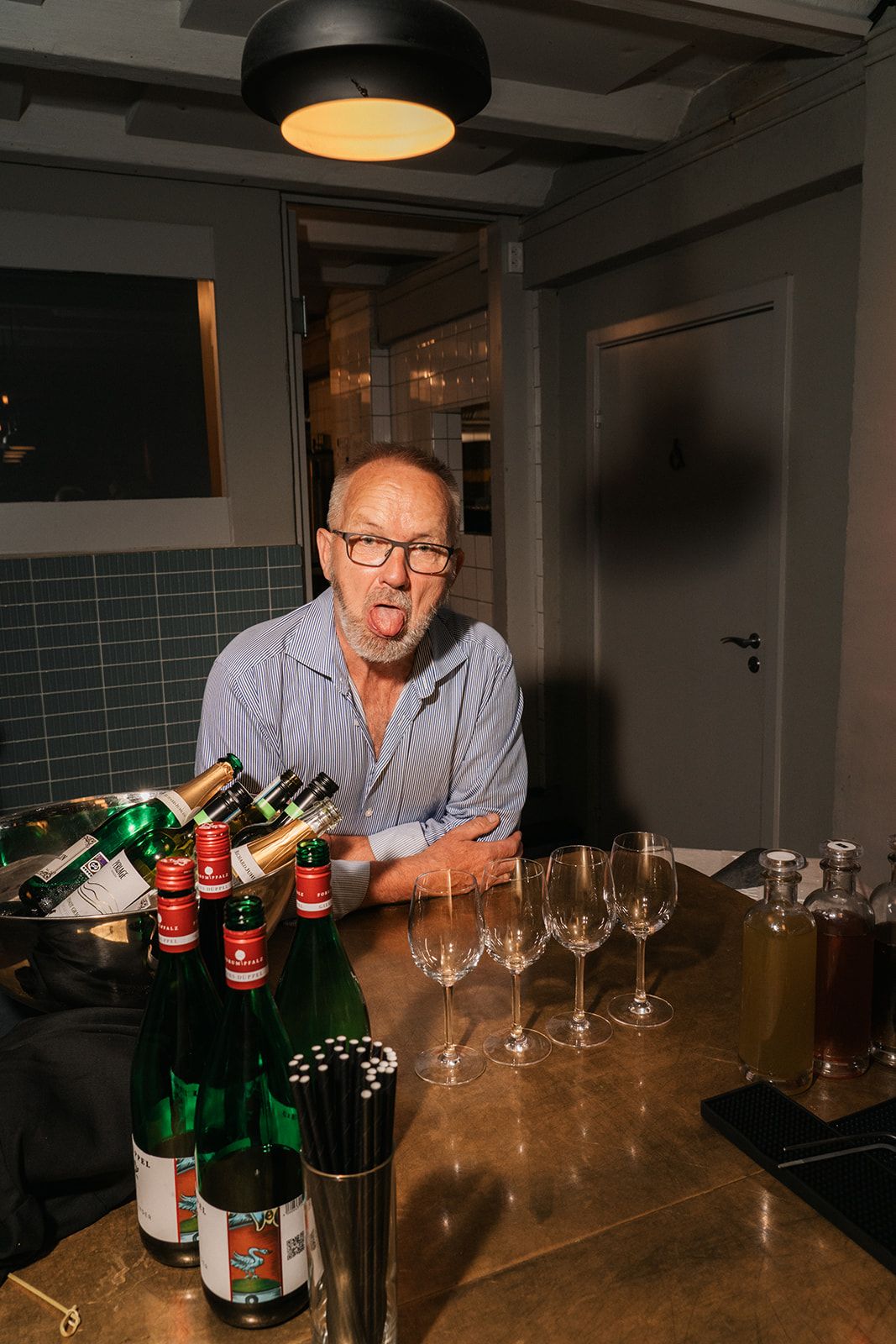 A sequence of photos showing a person gesturing with wine bottles and glasses on a wooden counter, taken at night.