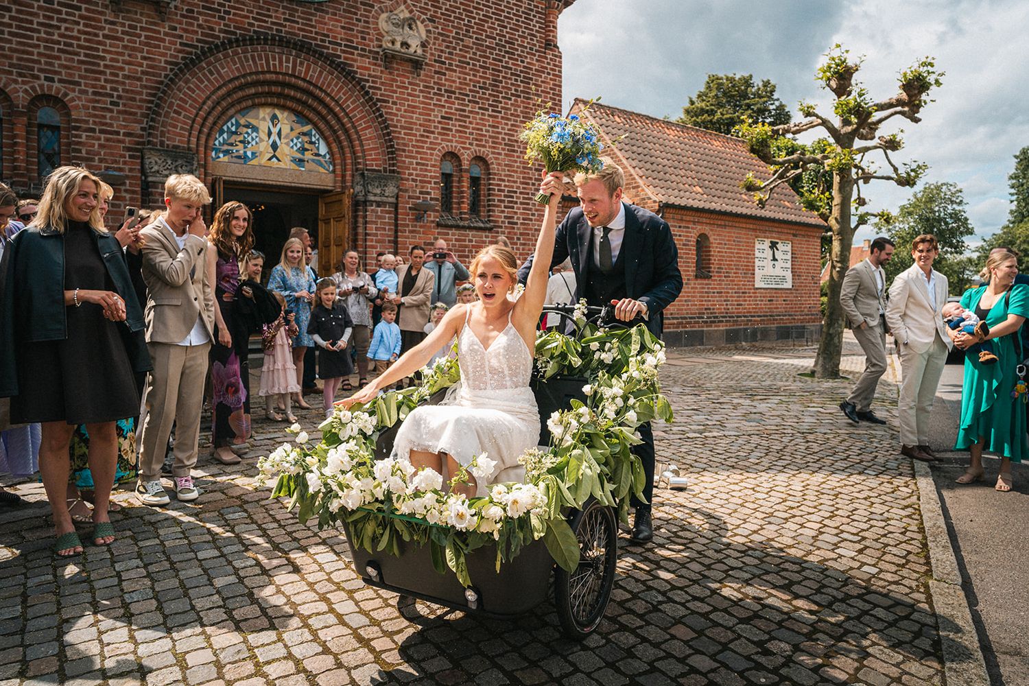 Wedding guests gathered outside a historic brick church with an arched entrance.