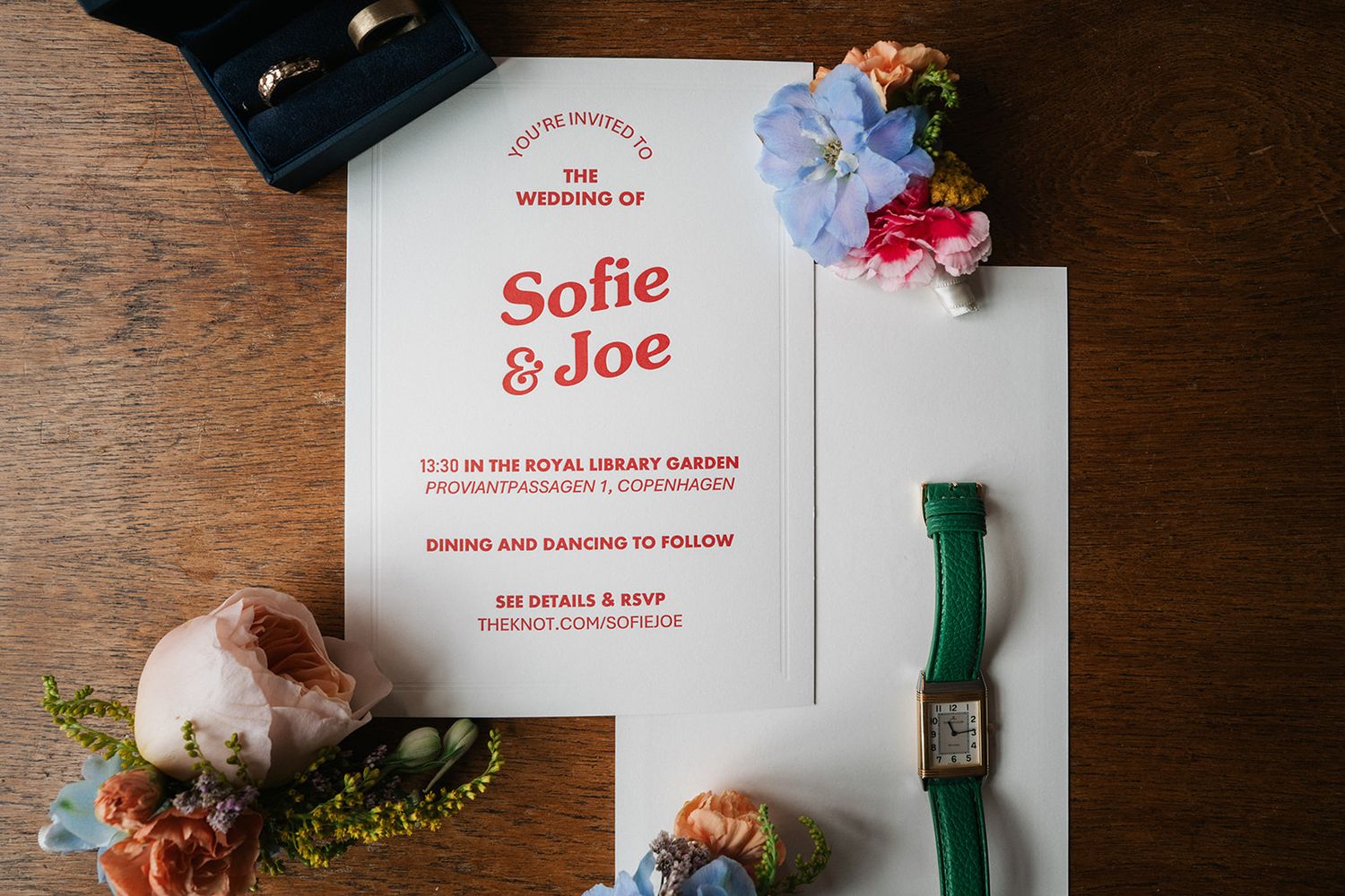 Wedding invitation card with floral decorations, green ribbon and wooden surface in flat lay composition.