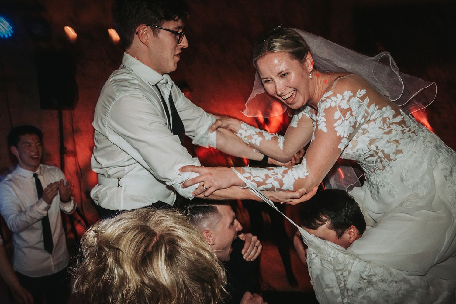 Wedding guests dance energetically on a dimly lit dance floor with vibrant red lighting in the background.