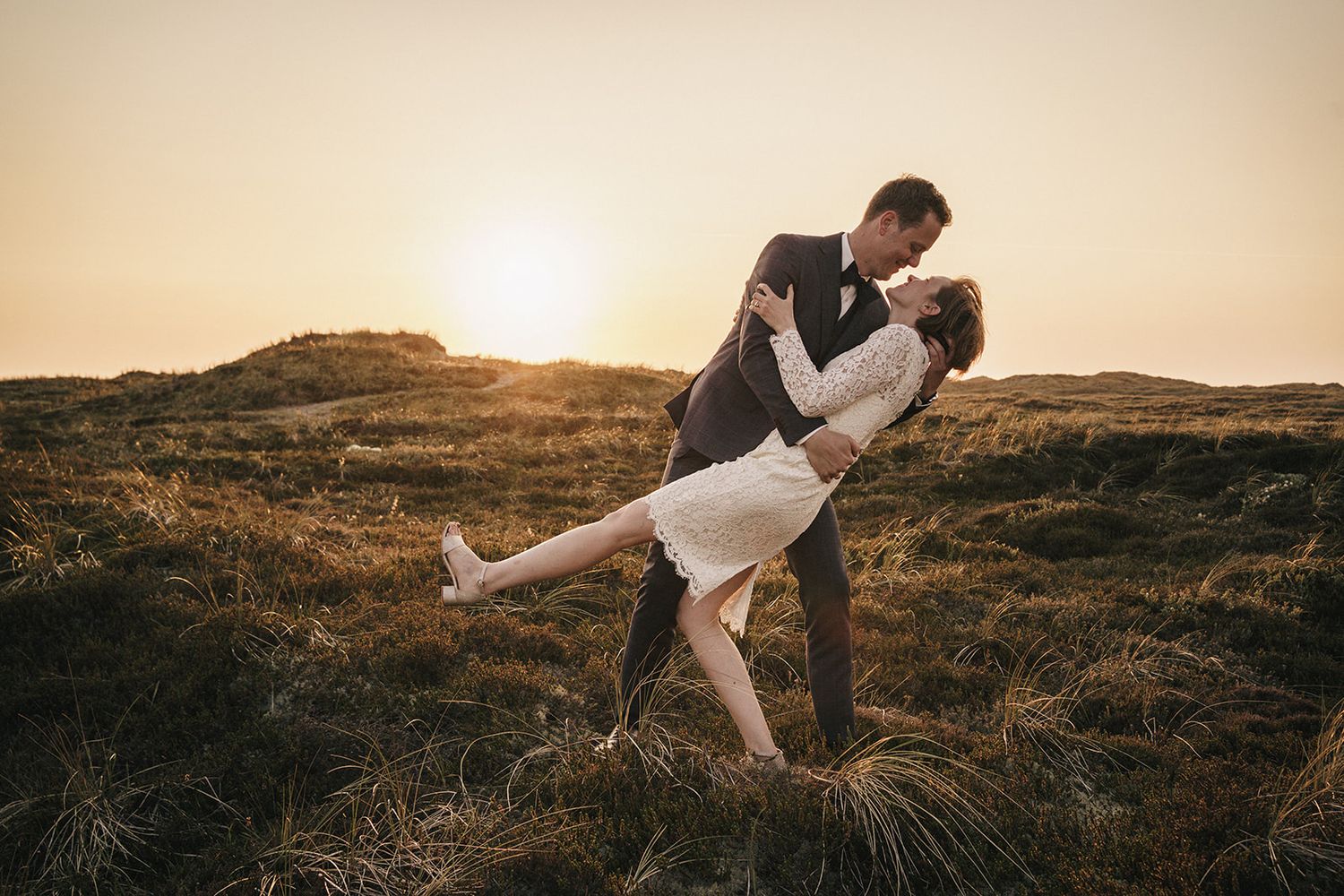 Romantic sunset photo of a couple embracing on a hilltop against a golden sky.