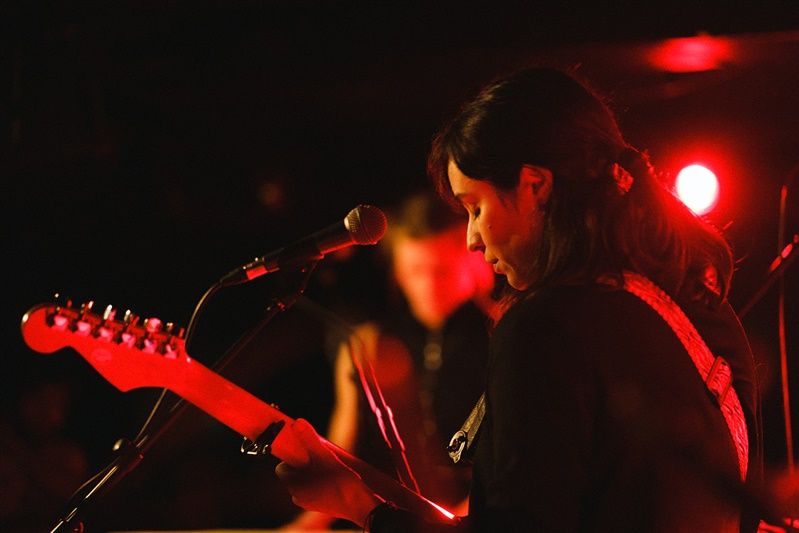Silhouetted musician performs on stage with red lighting and an electric guitar in the foreground.