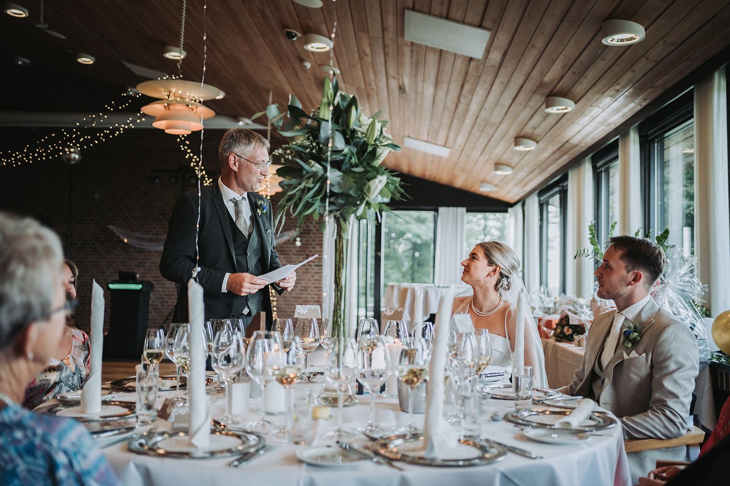 Wedding toast speech at elegant reception with candlelit table settings and wooden ceiling decor.