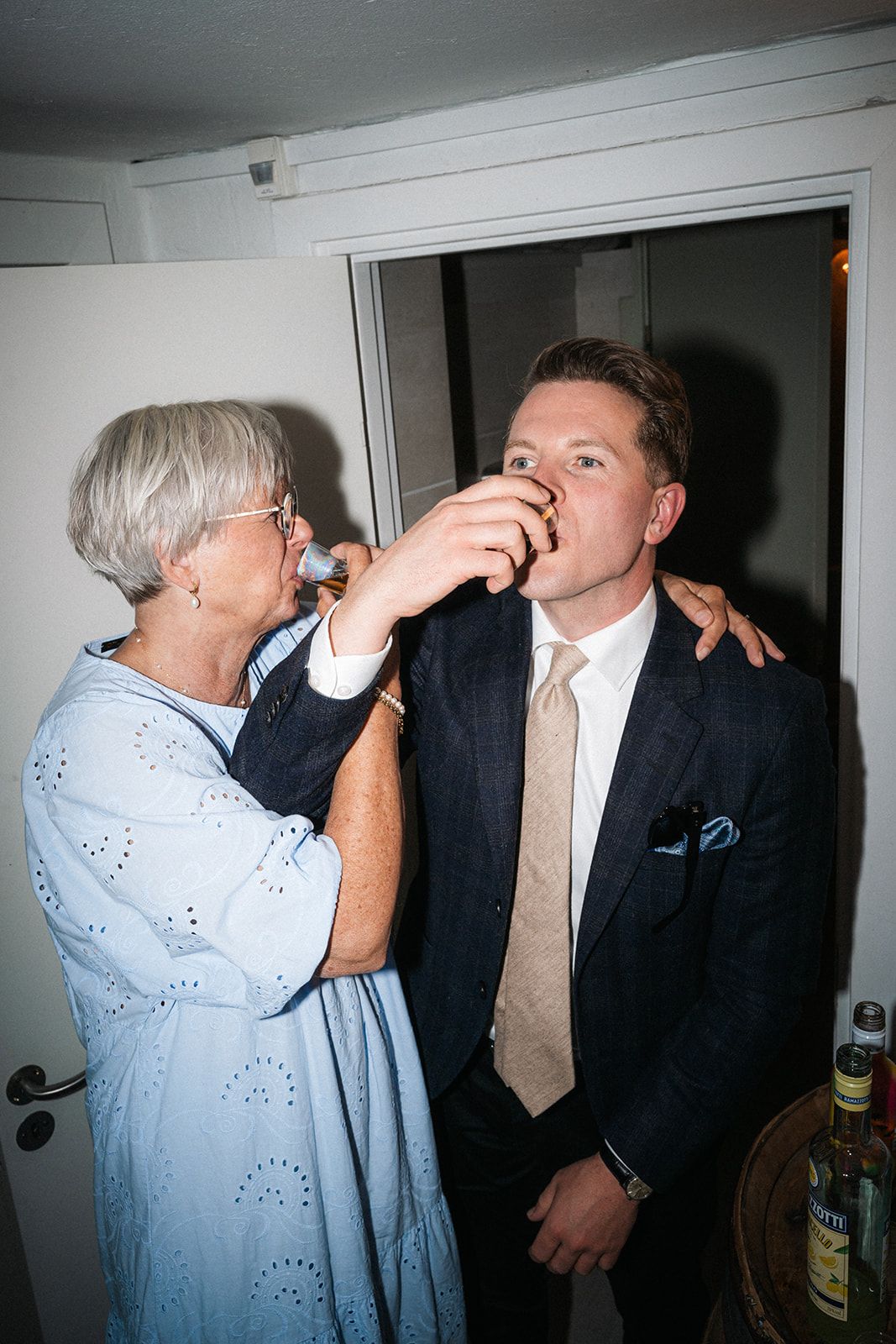 Two people in formal attire engage in drinking activity during what appears to be an indoor gathering or event.