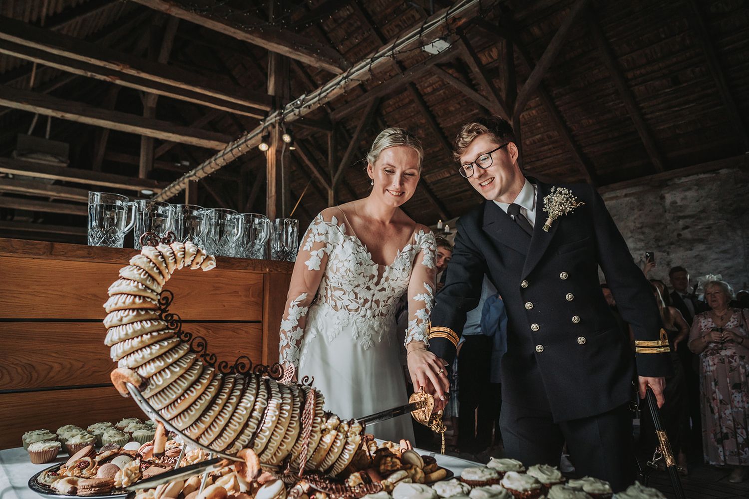 Two people stand beside an elaborate seafood display at a rustic wedding reception in a barn-style venue.