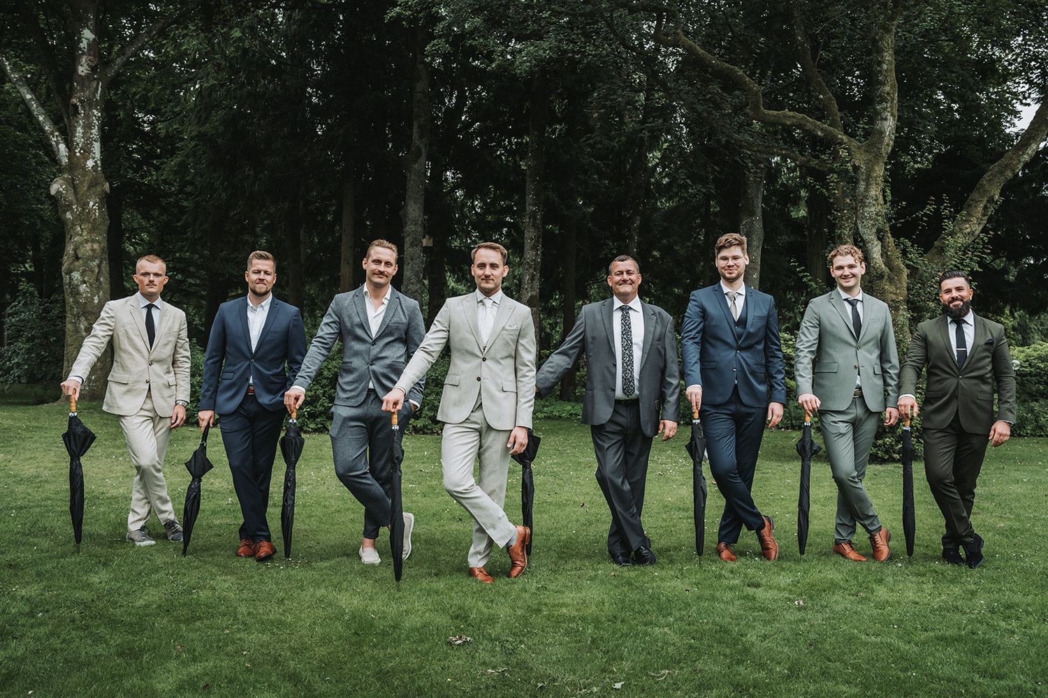 Group of wedding party members standing in a line posing together on a grassy lawn outdoors.