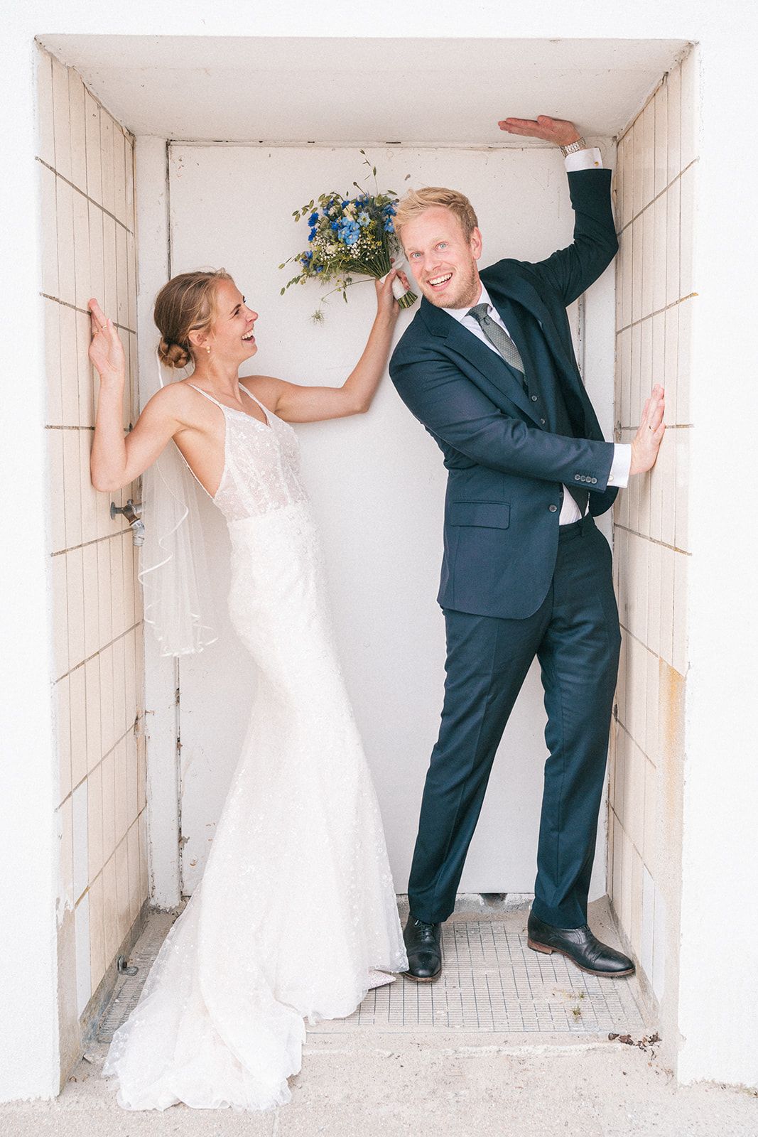 A fun wedding photo series showing a couple playfully pushing against white hallway walls in contrasting formal attire.
