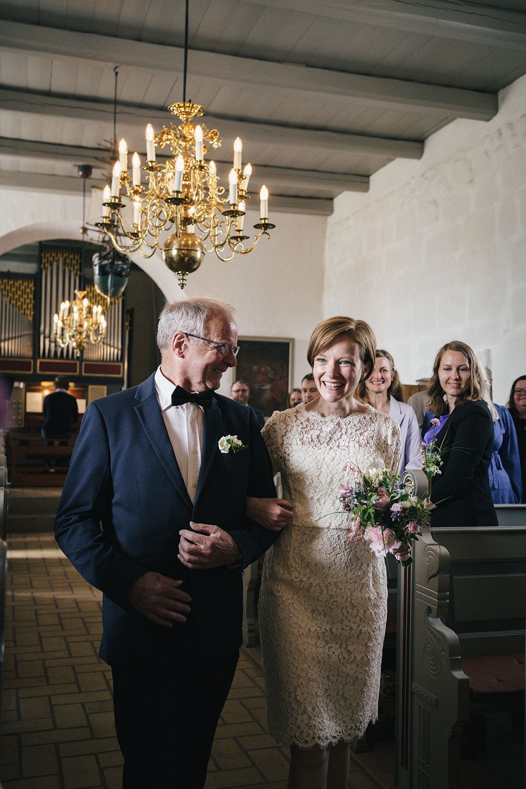Wedding ceremony in historic church interior with elegant brass chandelier and vintage organ.