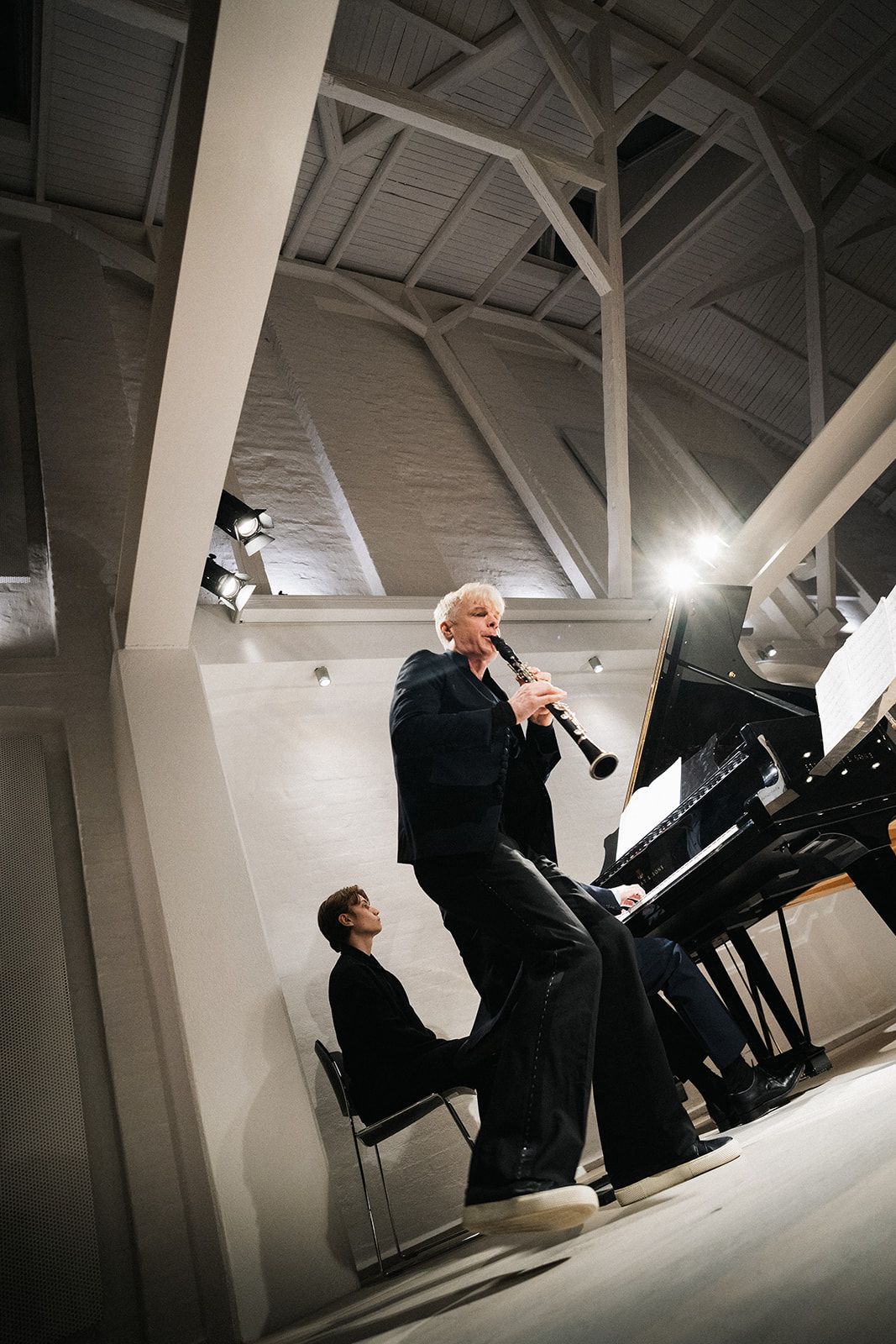 Dramatic side-view performance shots of pianist at black grand piano in white minimalist space with angular lighting.