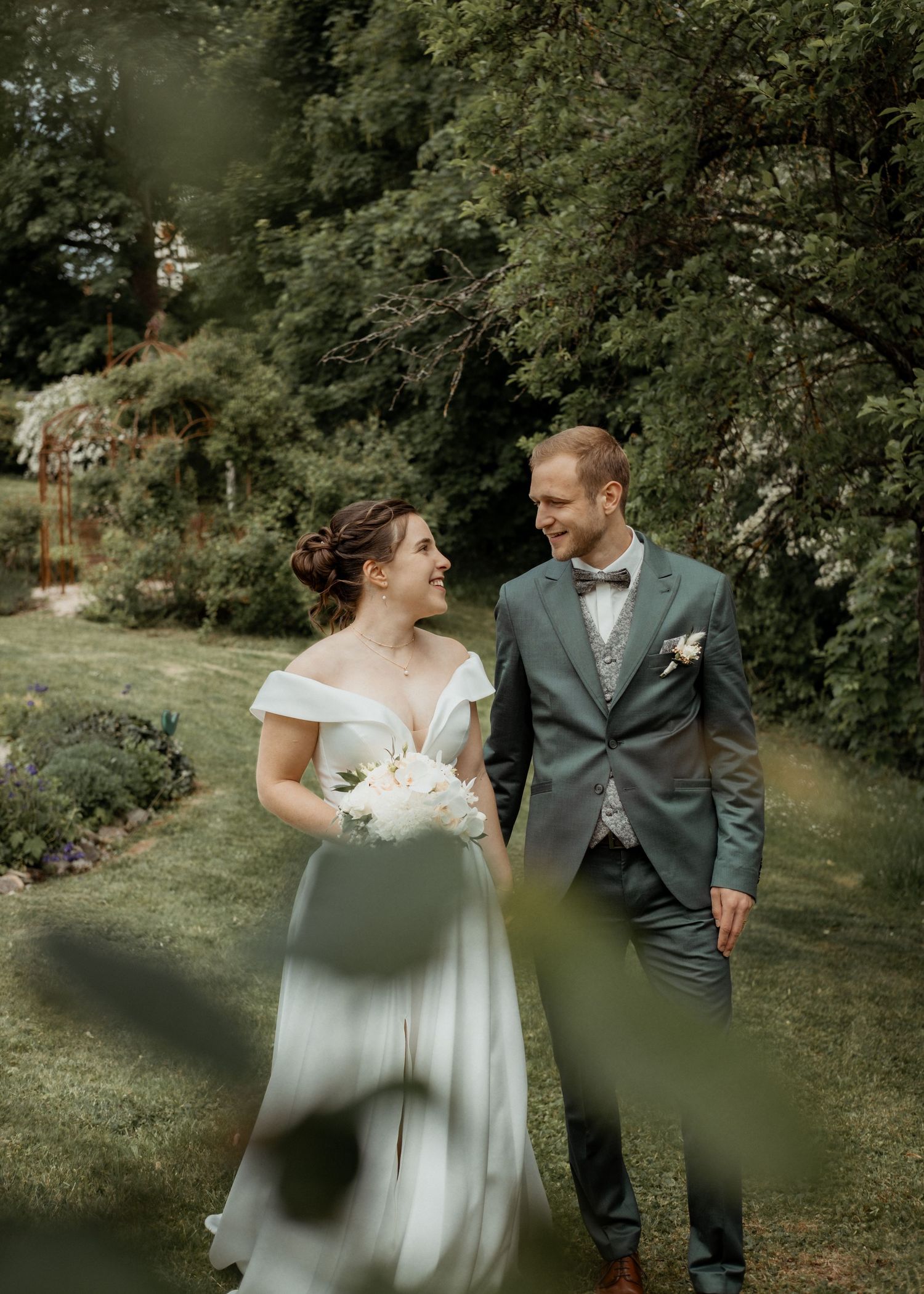 A couple in wedding attire walking together in a lush green garden setting.