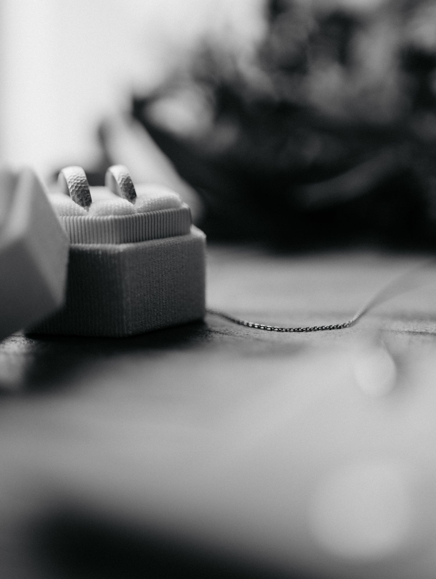 A black and white macro shot of a jewelry box with a necklace chain extending from it on a blurred surface.