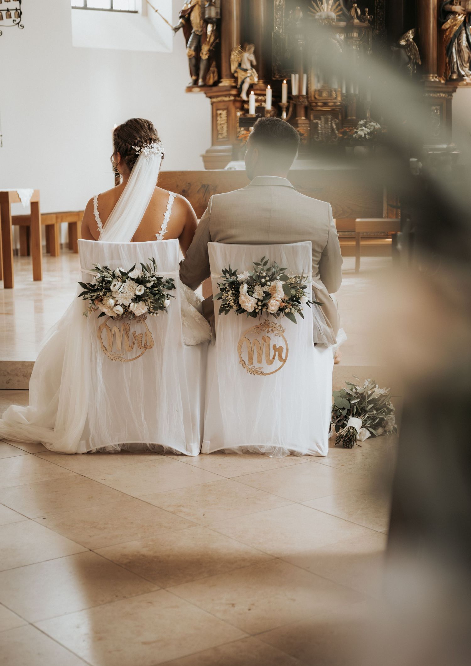 Wedding reception venue with white-covered chairs and floral arrangements in an elegant indoor setting.