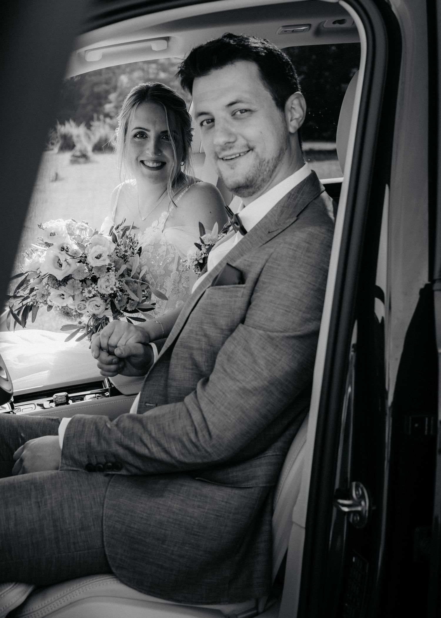 A couple in wedding attire sit together in a vintage car, captured in black and white across multiple candid moments.