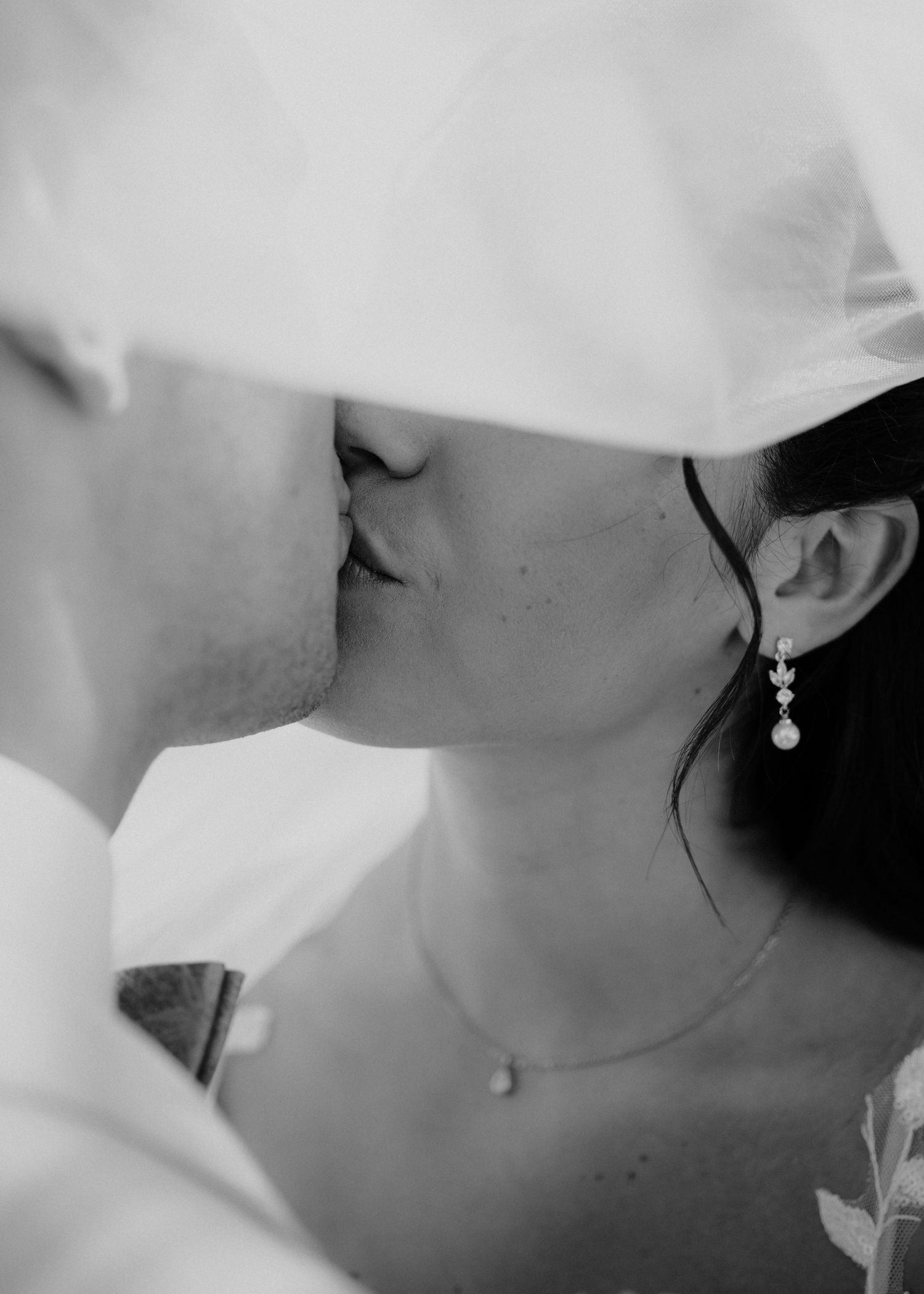 Black and white photo of a bride and groom sharing a romantic kiss under a wedding veil.