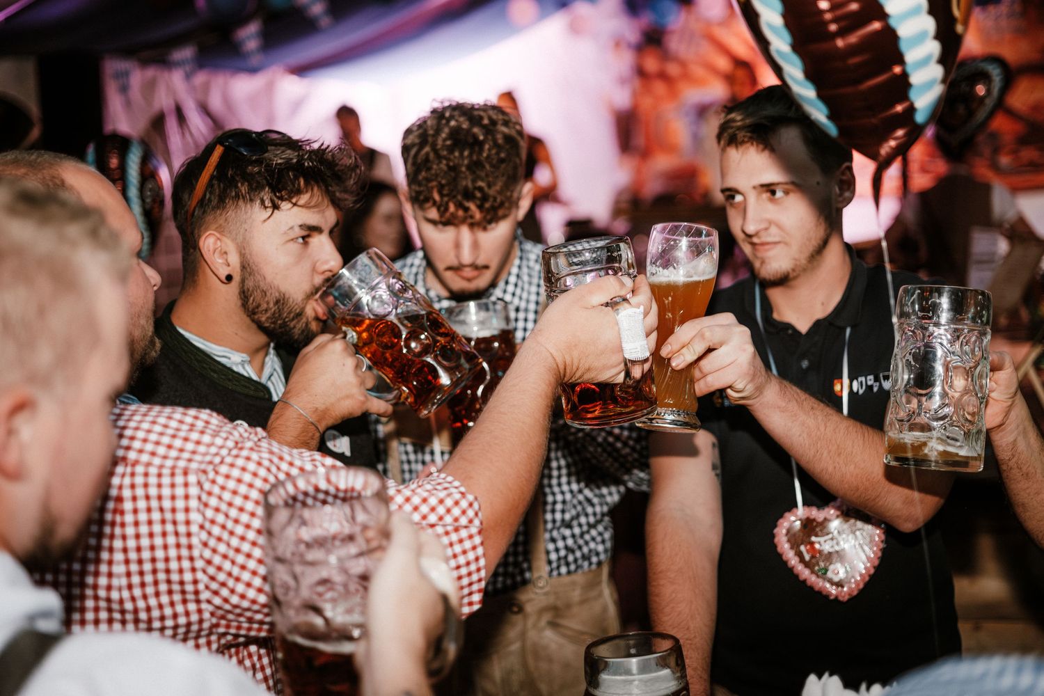 Friends in traditional Bavarian outfits toasting with beer steins at what appears to be an Oktoberfest celebration.