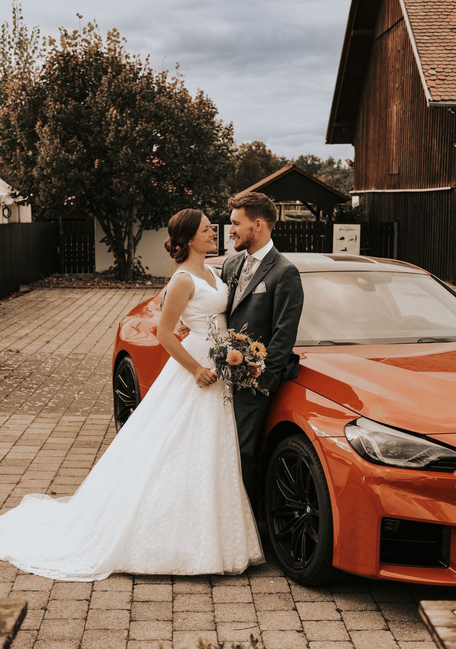 A romantic wedding scene features a flowing white gown next to a sleek orange sports car on a stone patio.