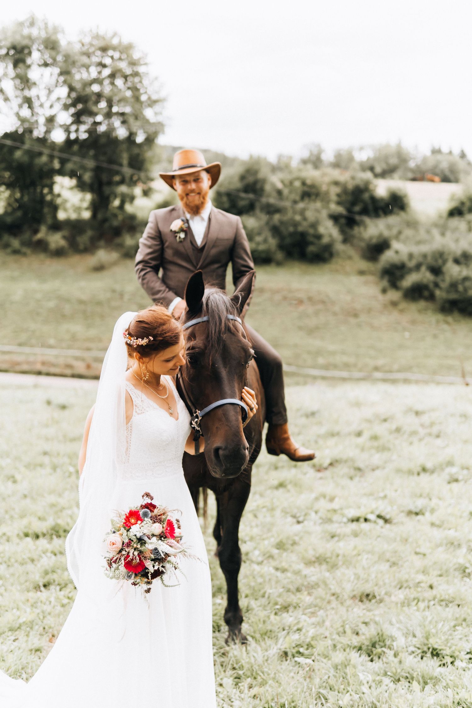 A romantic wedding photoshoot in a grassy field with a beautiful black horse and elegant floral bouquet.