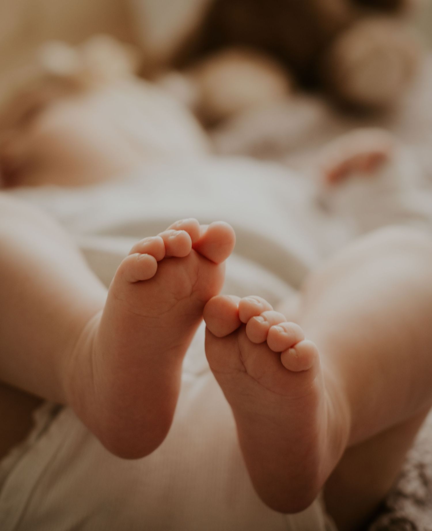 Close-up view of tiny baby feet with soft wrinkles and delicate toes against a light background.