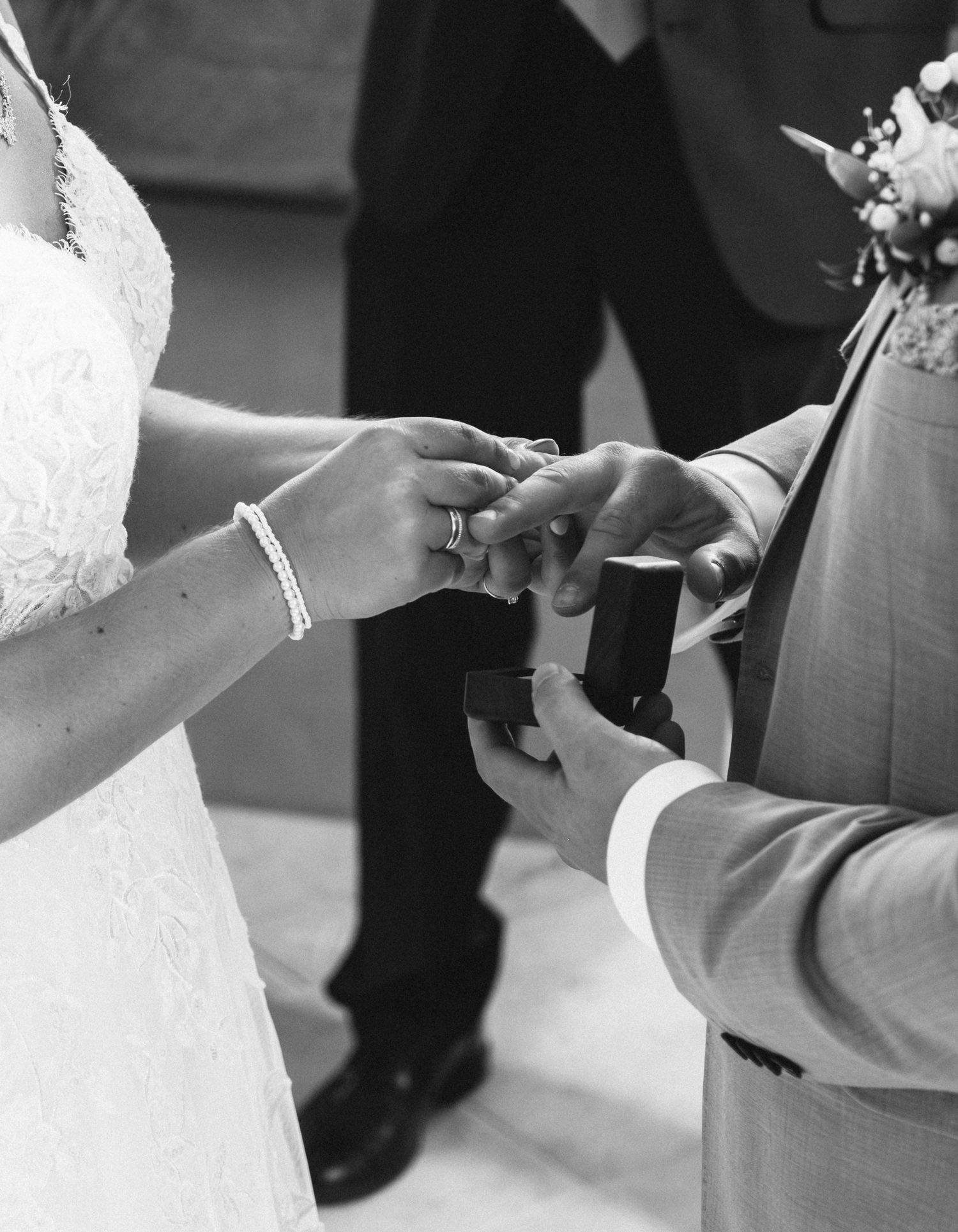 Black and white photo showing hands exchanging wedding rings during a traditional ceremony.