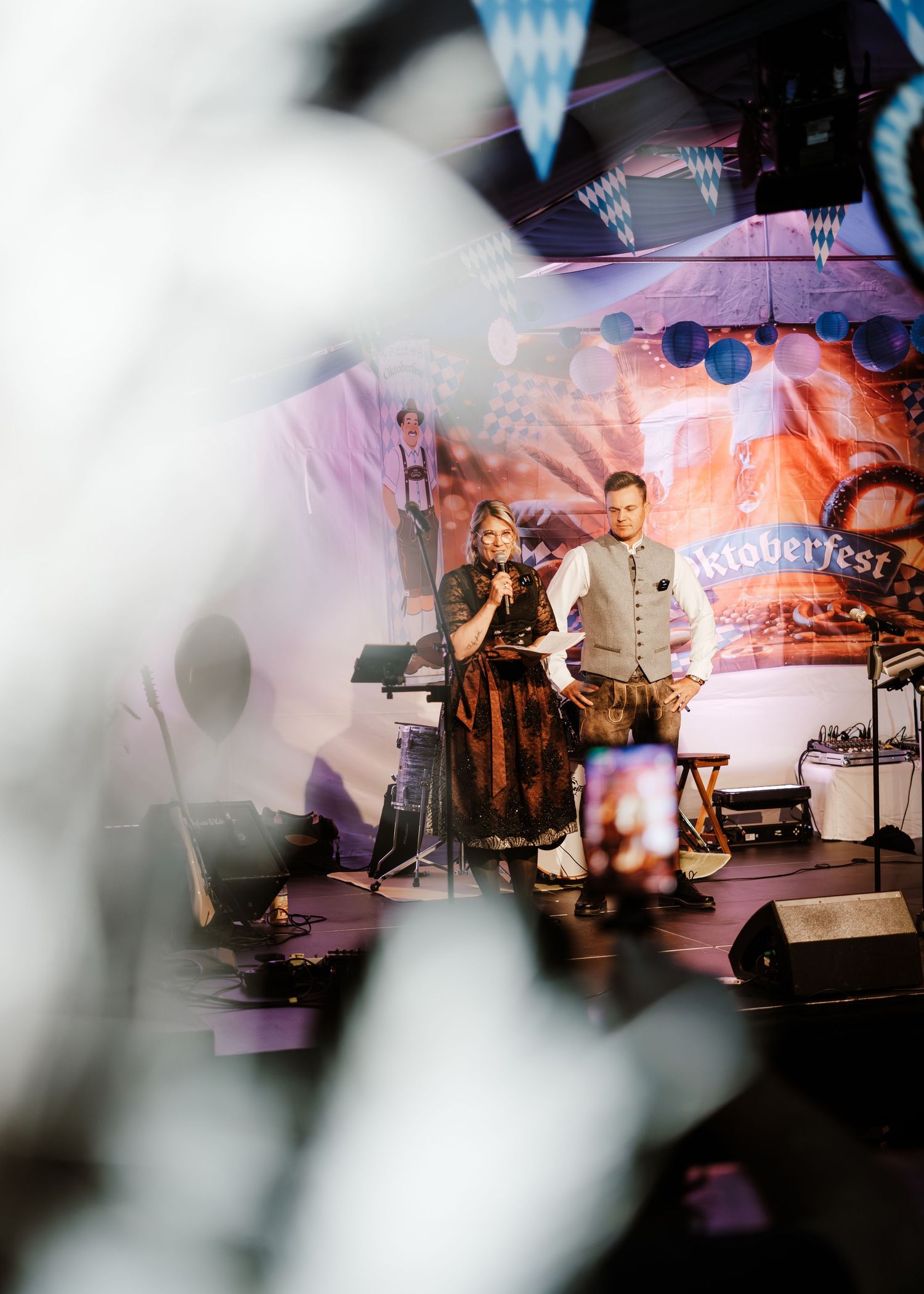 Musicians perform on stage at an Oktoberfest celebration with blue and white decorations and atmospheric lighting.