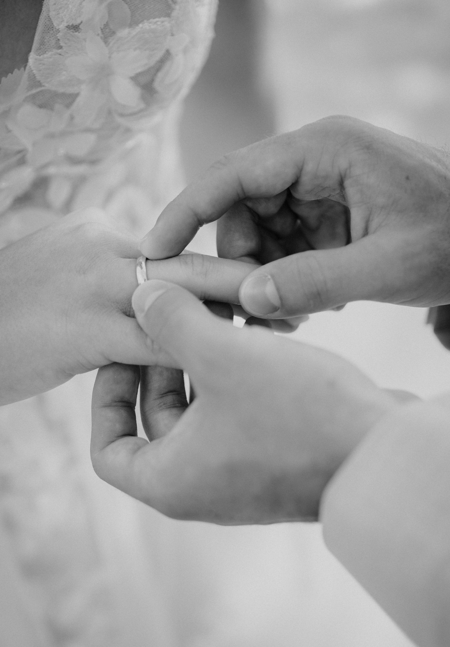 Black and white photo of a groom placing a wedding ring on the bride's finger during a ceremony.