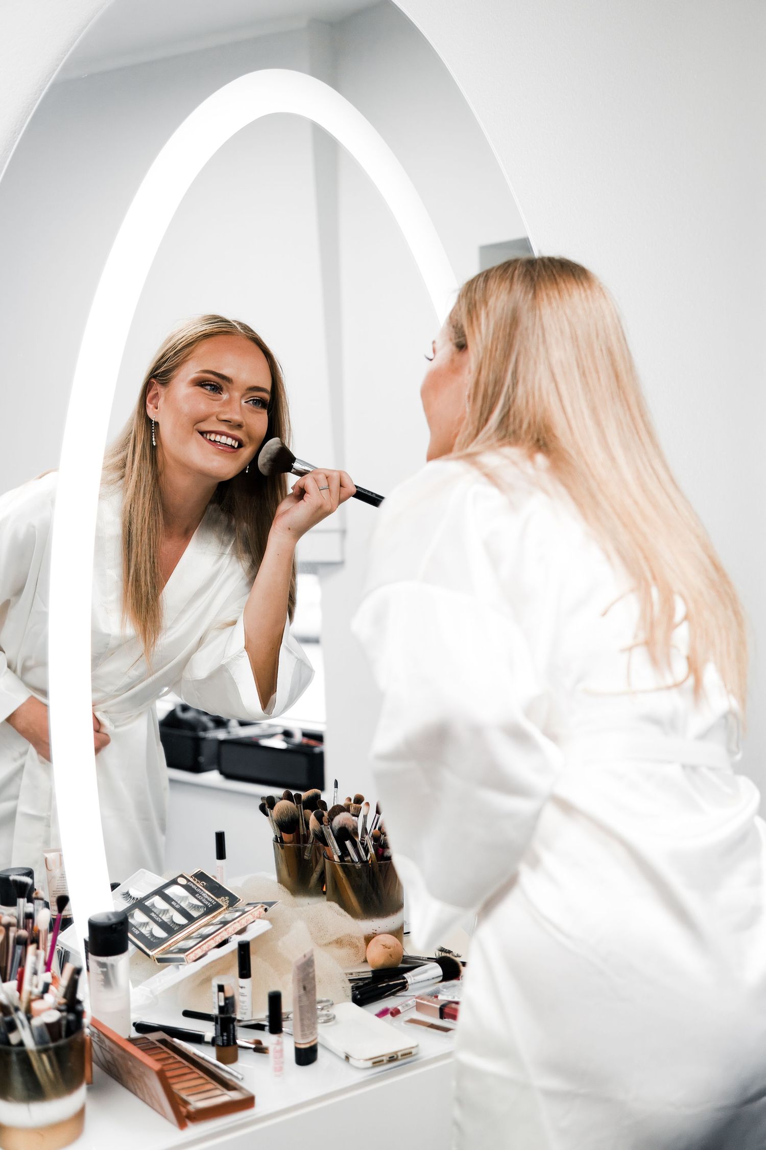 A series of photos showing a person in a white blazer applying makeup at a vanity table with cosmetics and brushes.