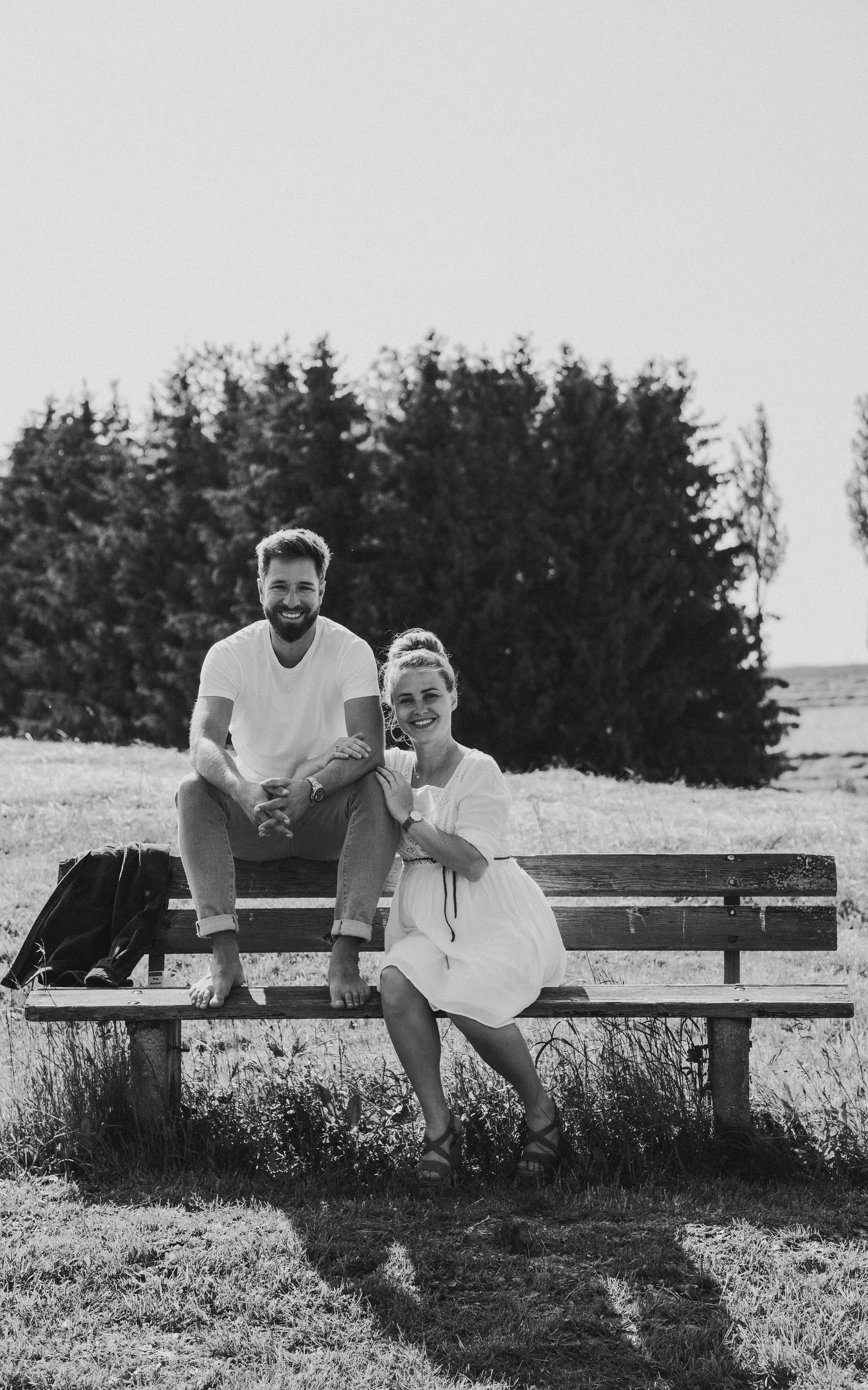 A black and white photo sequence shows a playful couple lounging and interacting on a wooden bench outdoors.