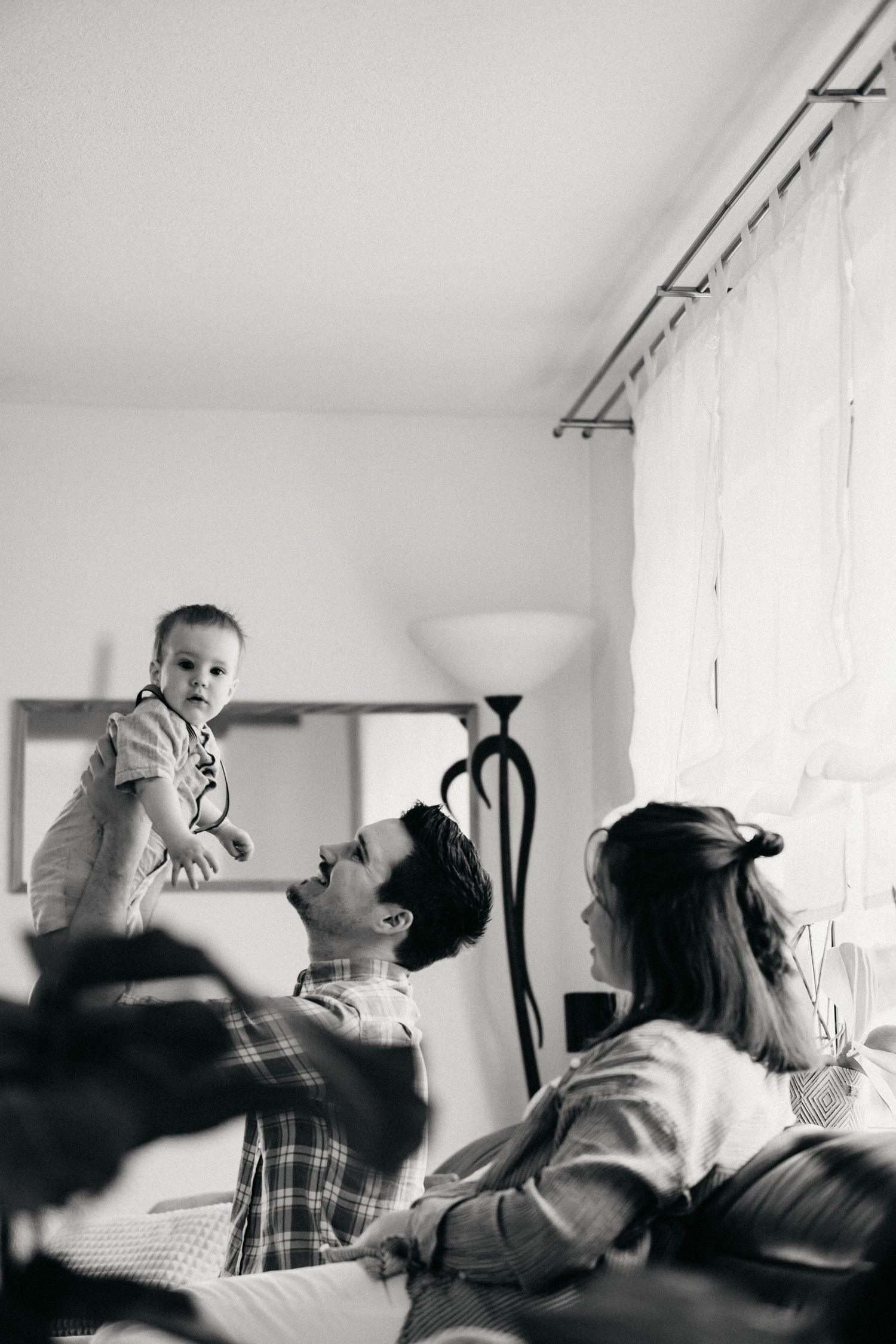 A black and white candid family moment showing a relaxed scene on a couch in a bright living room.