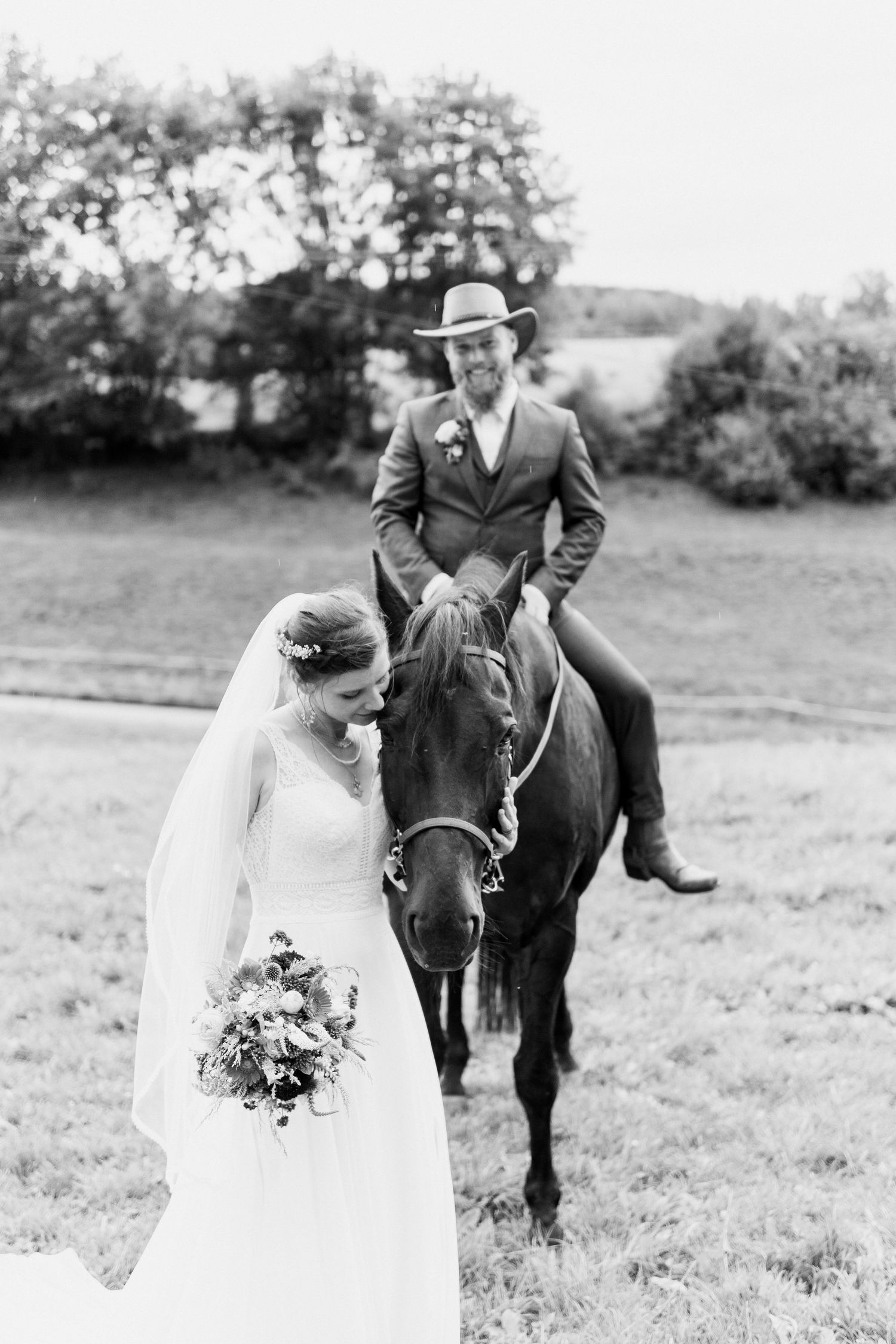 Black and white wedding photos showing couple posing with horse in field during outdoor countryside celebration.