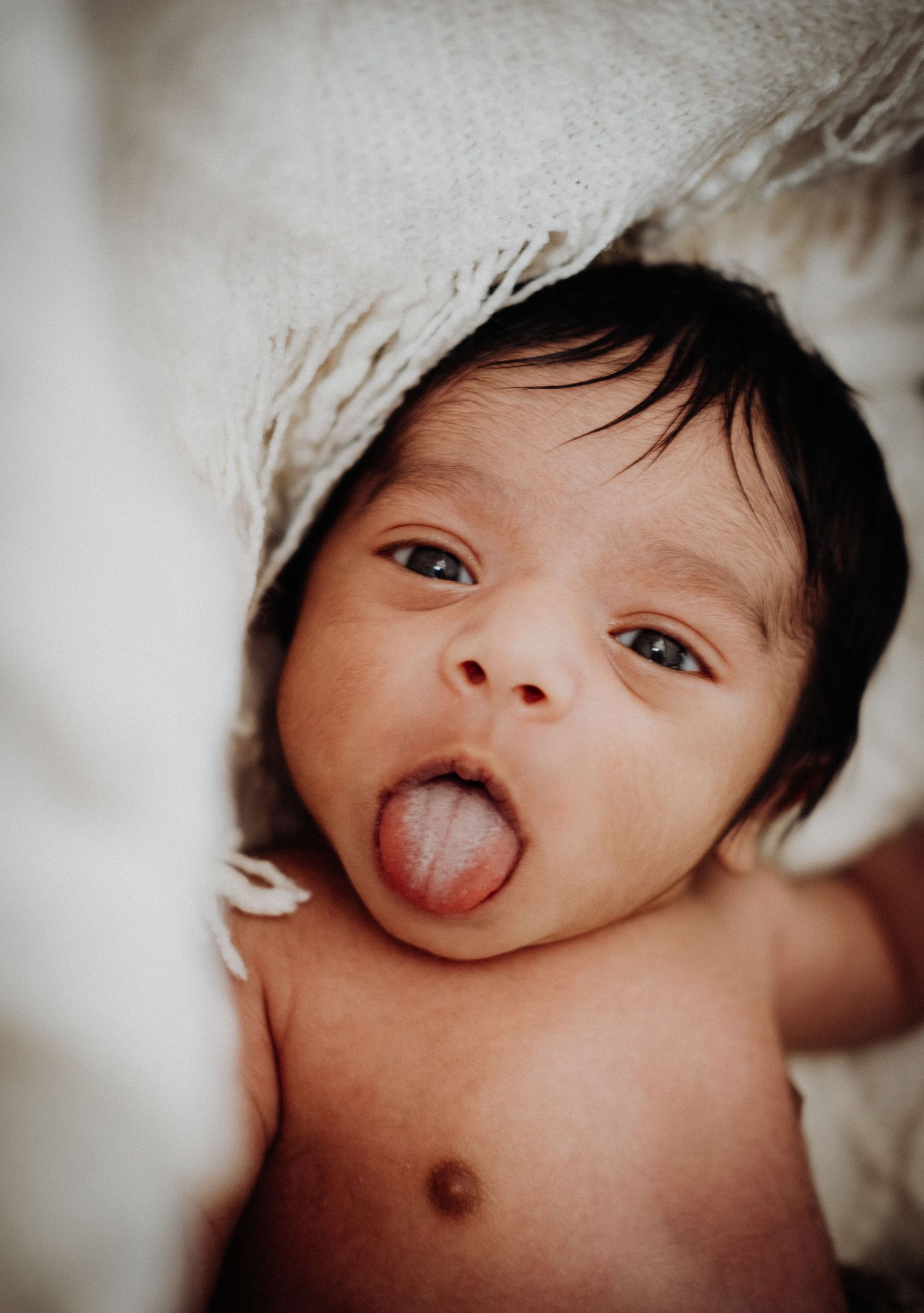 A series of close-up photos showing a baby making silly faces and sticking out their tongue while lying down.