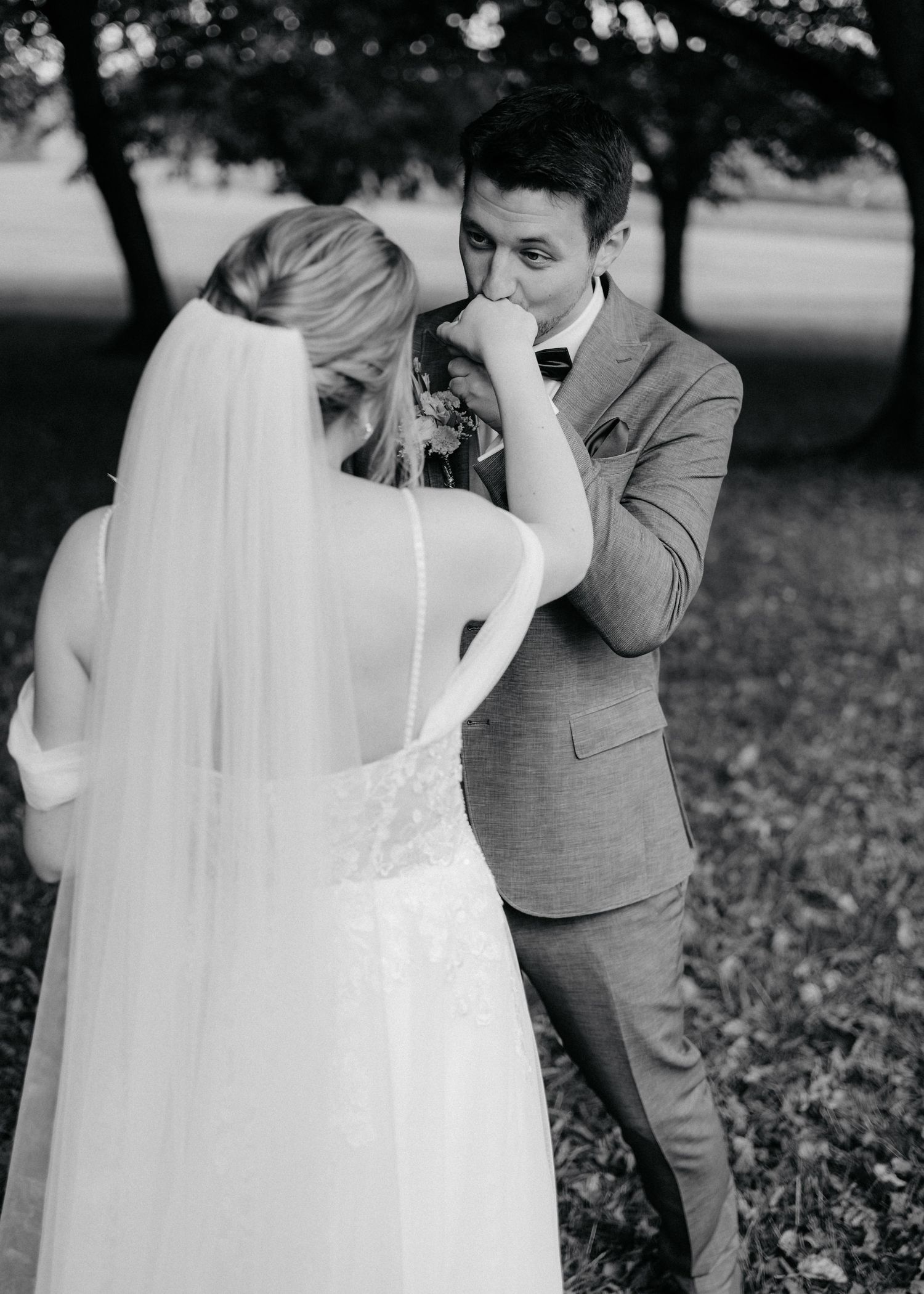 A tender black and white wedding moment captured outdoors as a couple shares an intimate moment under trees.
