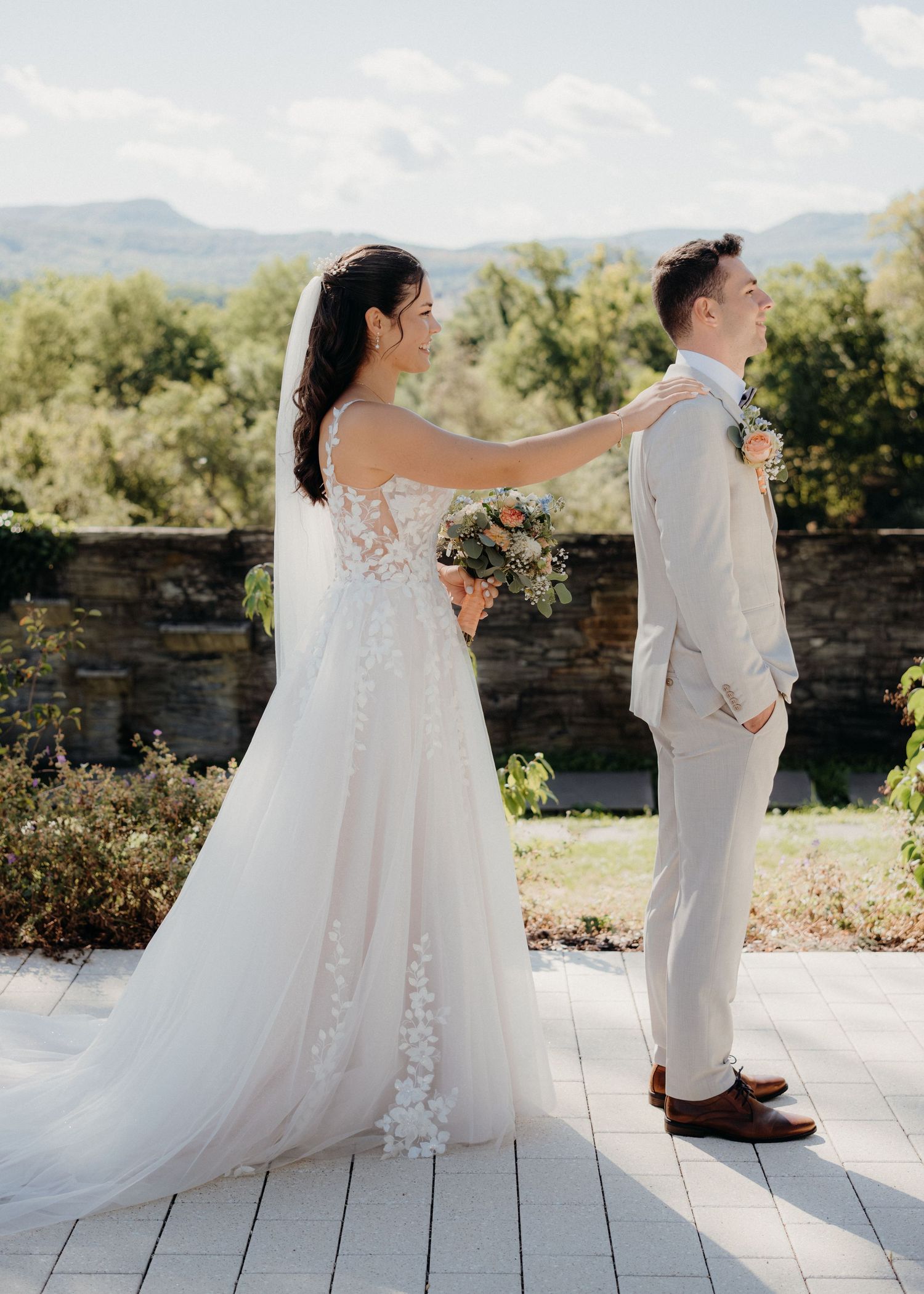Bride adjusting groom's suit collar during first look at outdoor wedding venue with mountain views.