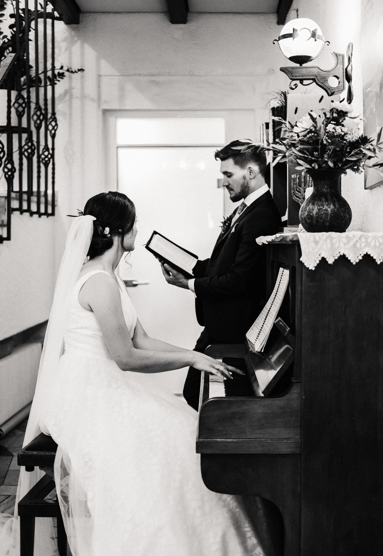 A black and white wedding ceremony photo showing a couple at a piano during an intimate indoor service.