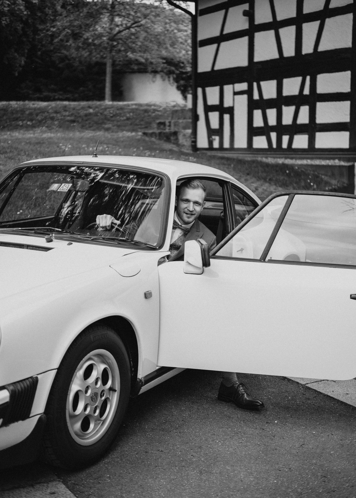 Vintage black and white photo of a classic car parked in front of a half-timbered building.