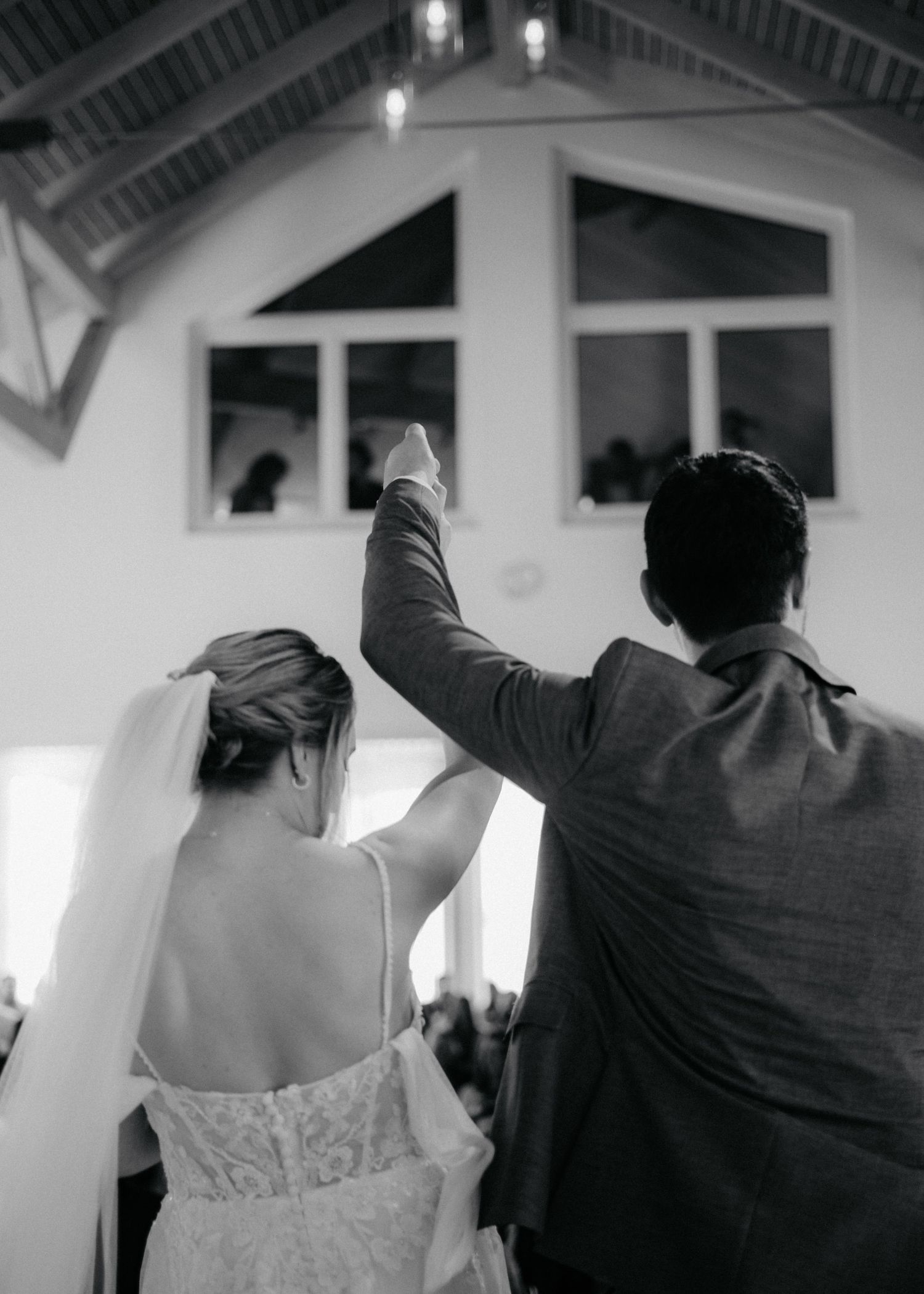 A sequence of wedding guests with their backs turned performing a synchronized dance move with raised arms in a church.