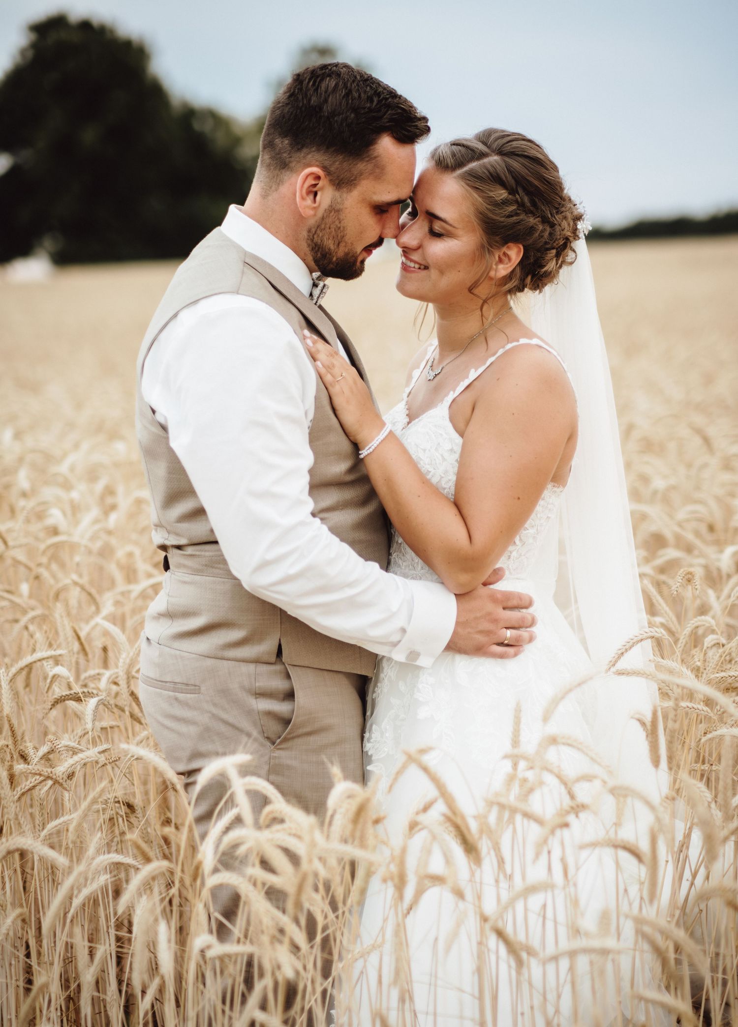 A romantic wedding couple embraces tenderly in a golden wheat field during their countryside photo session.