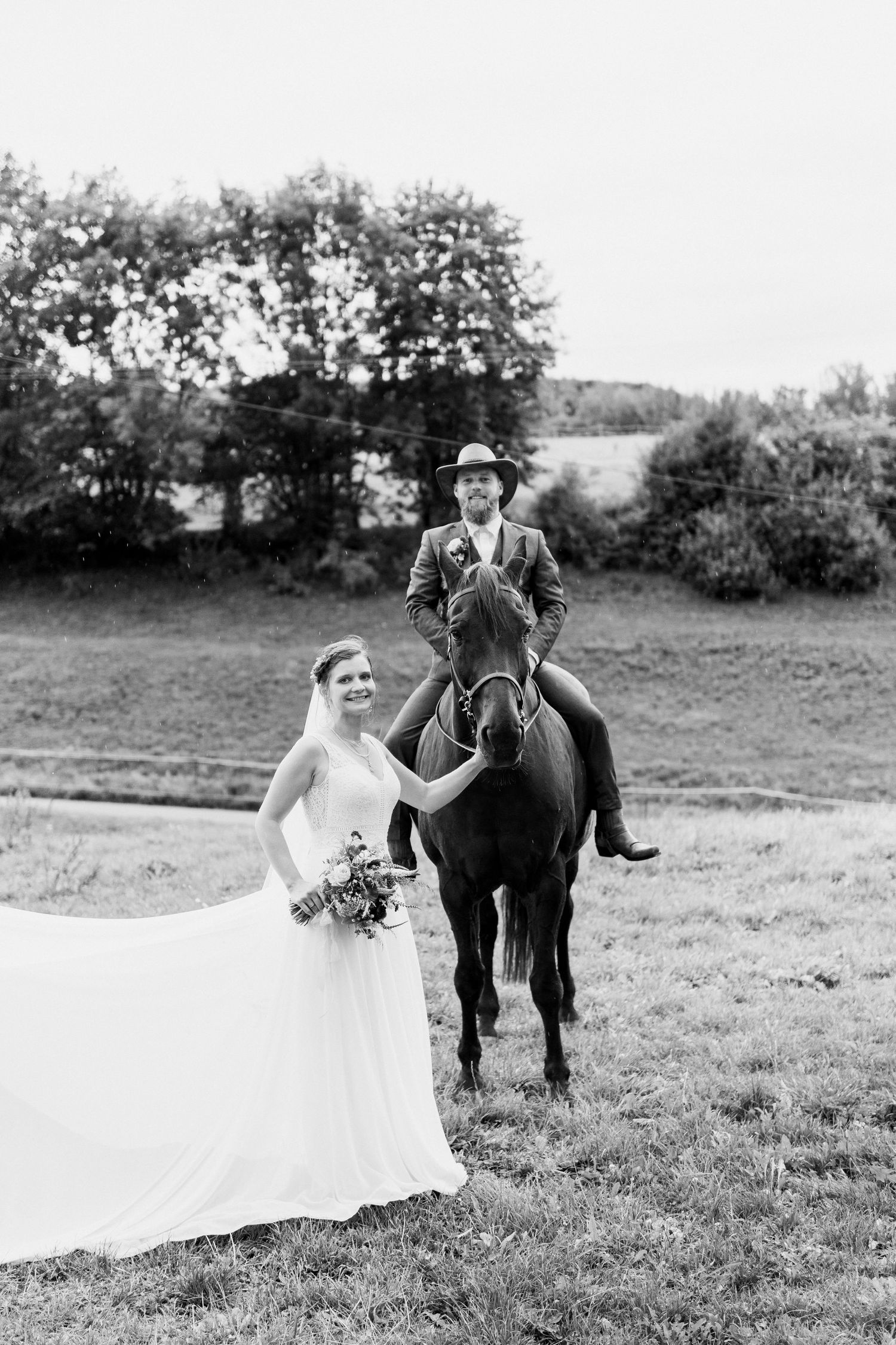 A couple poses with their horse in a grassy field during a black and white wedding photoshoot.
