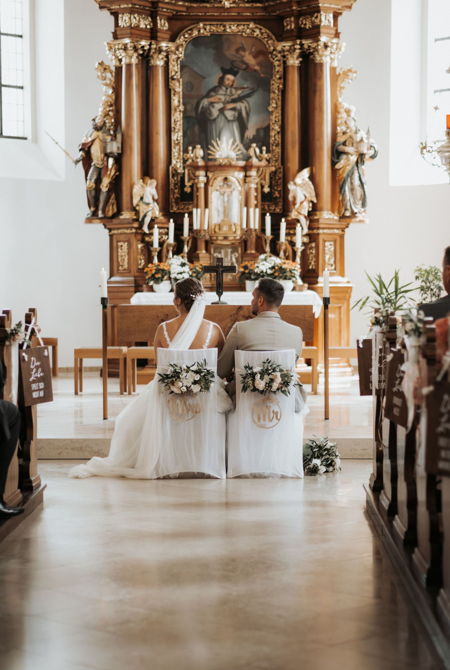 Beautiful church interior with ornate wooden altars and white floral decorations during an elegant wedding ceremony.