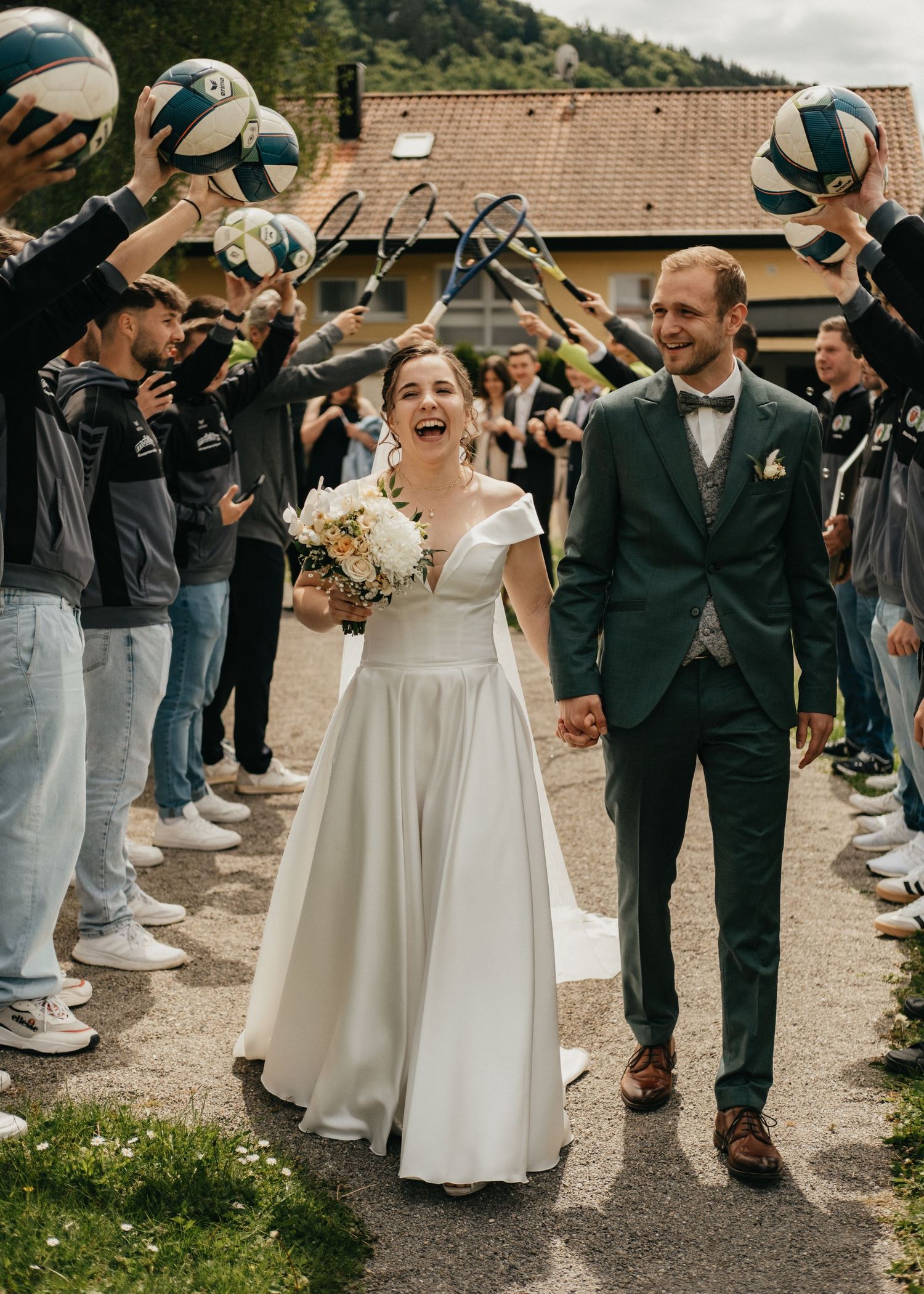 Wedding party forms celebratory tunnel for newlyweds outside rustic venue.