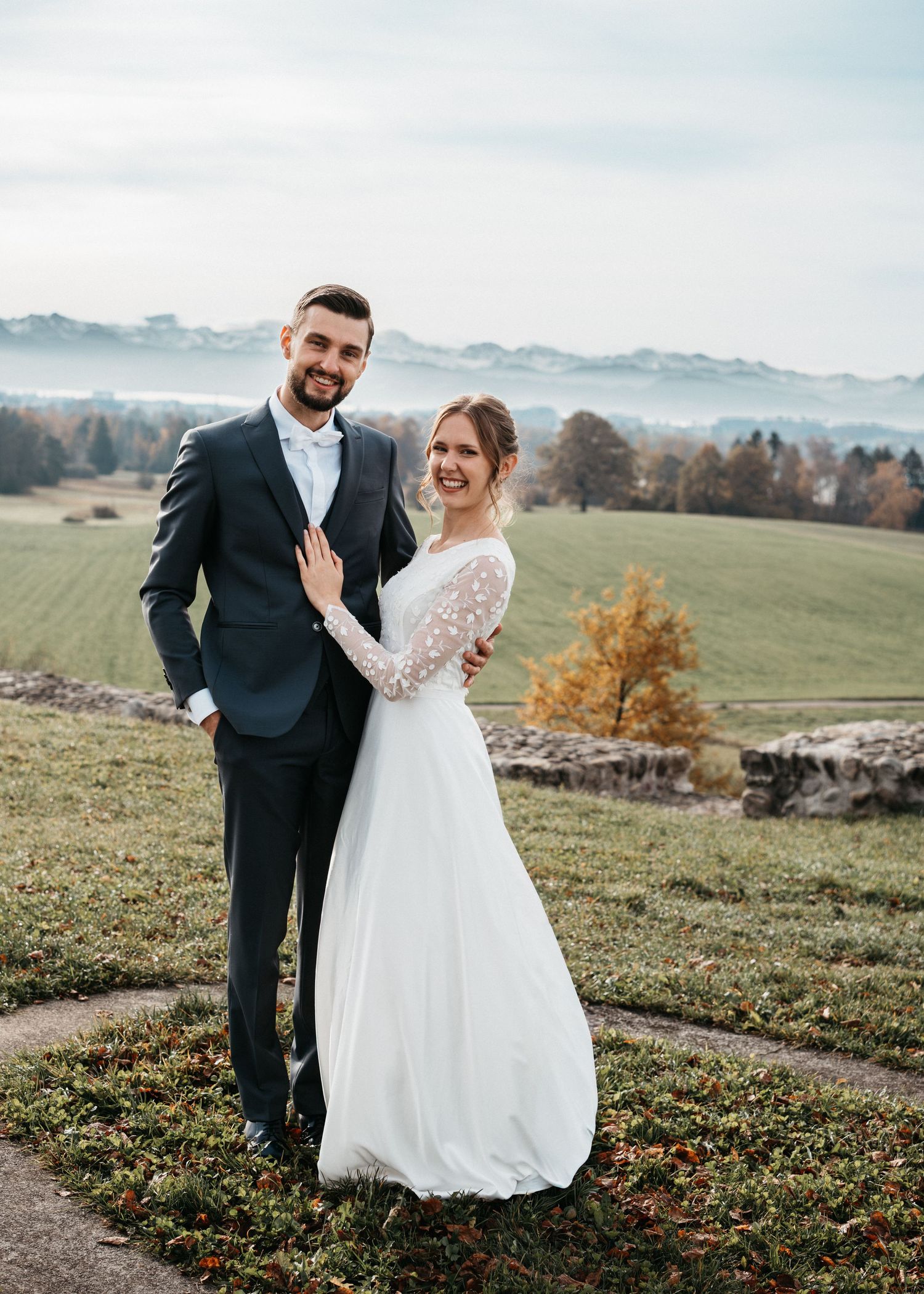 A newlywed couple poses together on a hilltop overlooking misty autumn landscapes with golden trees in the background.