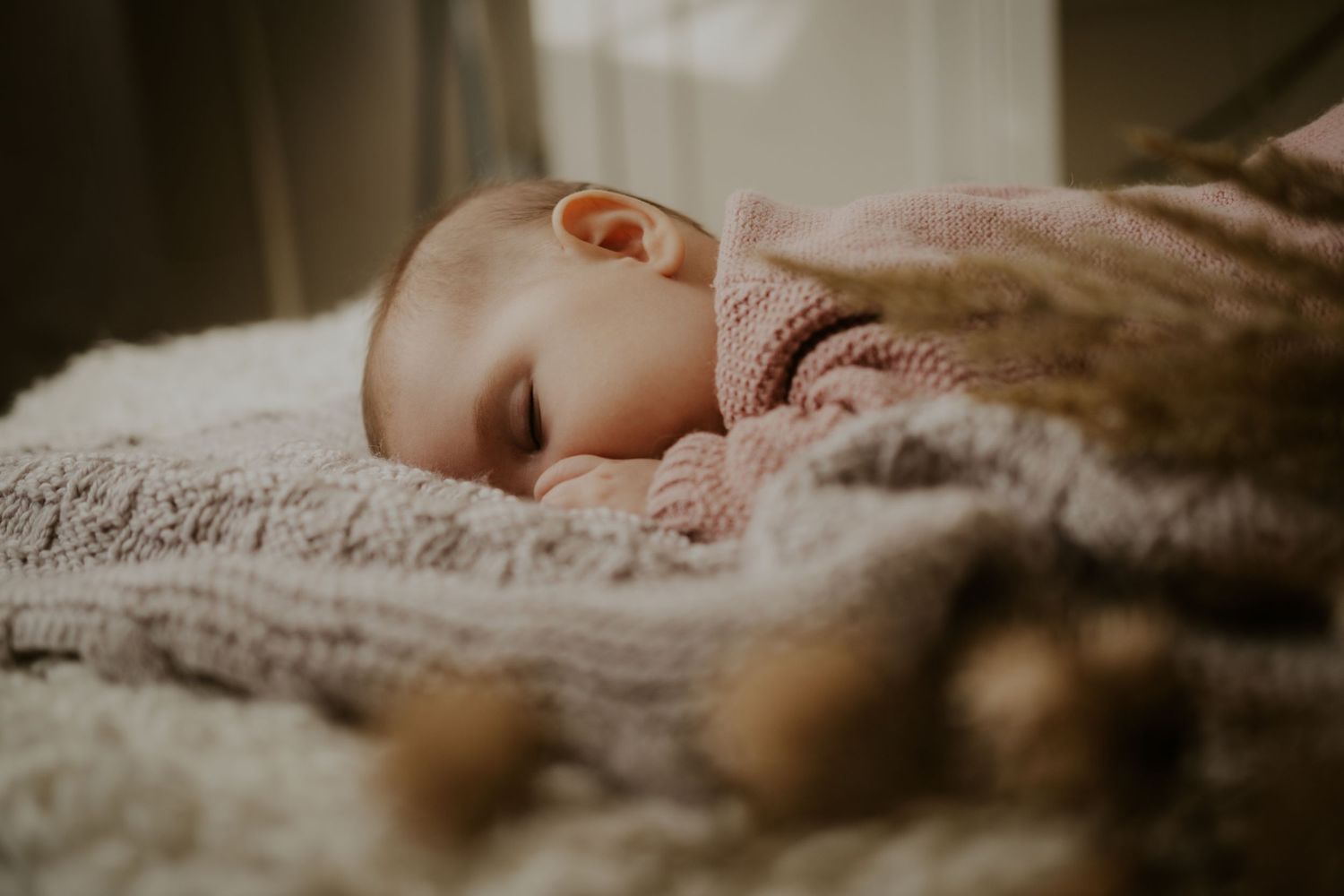 Close-up profile view of a baby sleeping on a cozy knitted blanket in soft lighting.