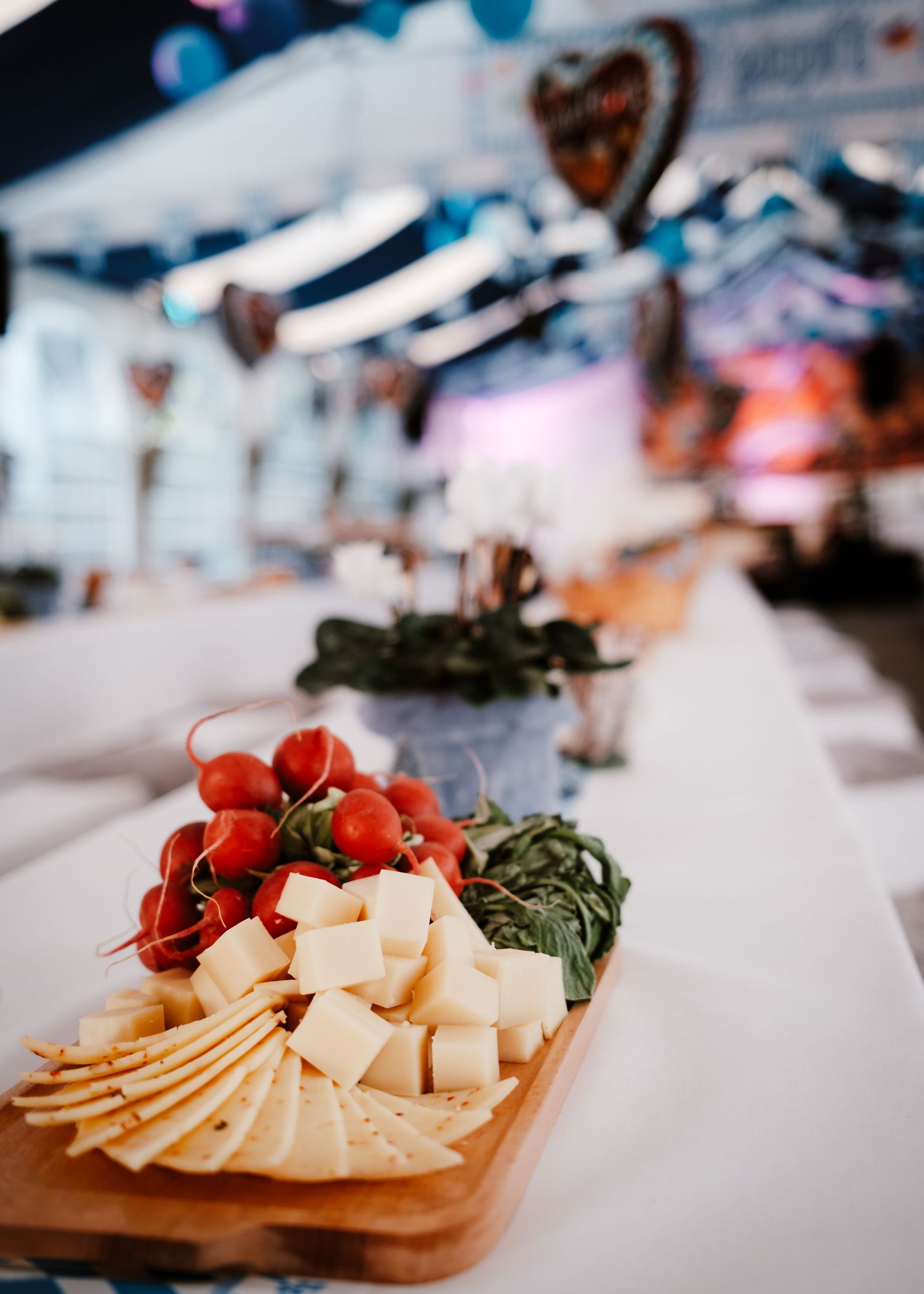 A wooden charcuterie board displays an artfully arranged assortment of sliced cheeses and fresh red tomatoes.