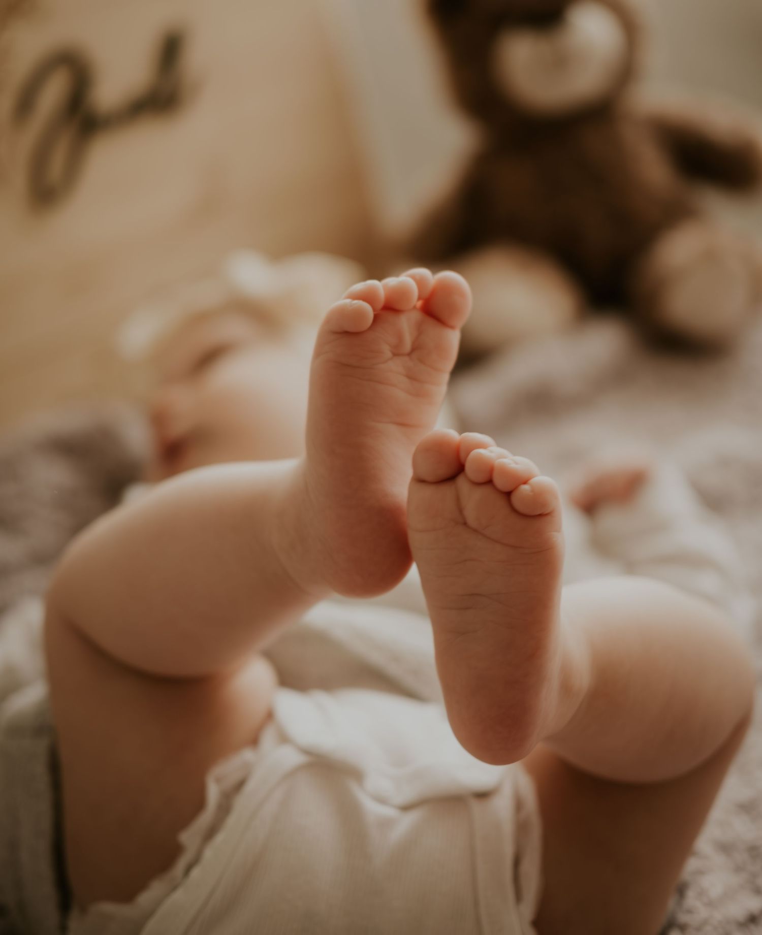 Close-up view of tiny newborn baby feet against a soft white blanket in warm natural lighting.